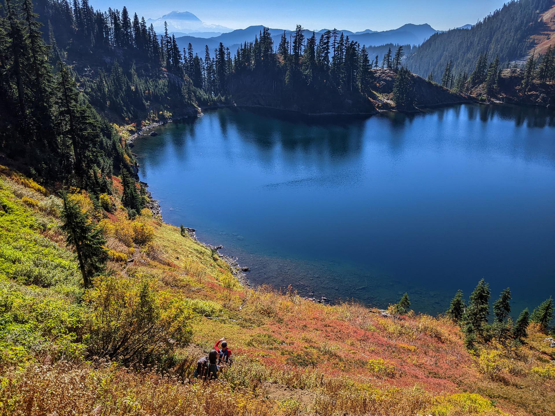 Person sitting on a colorful autumn hillside overlooking a vast blue lake and forests.