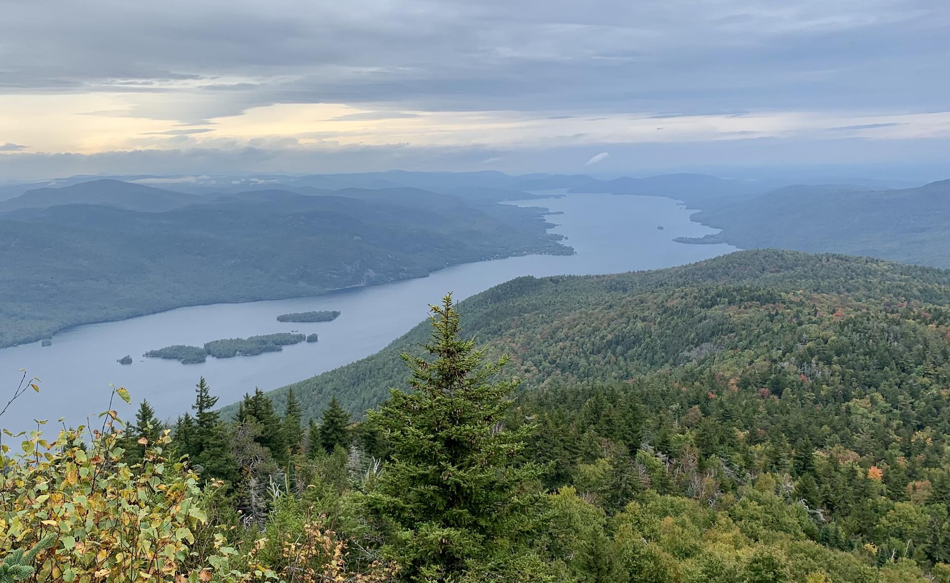 Overcast view of a large lake winding through forested mountains.