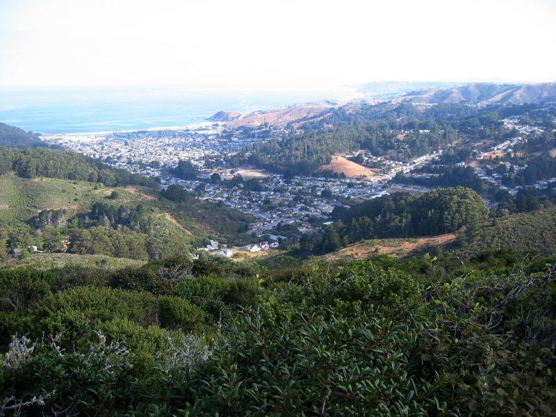 An aerial view of a coastal town nestled in green hills by the ocean.