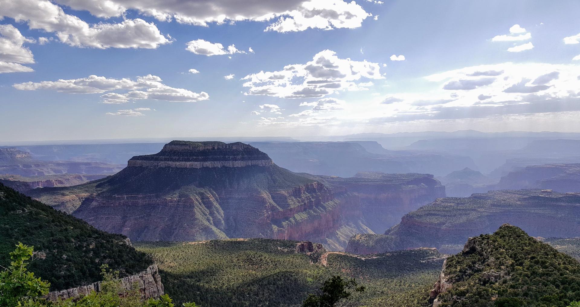Majestic flat-topped mountain overlooks hazy canyons under a cloudy sky.