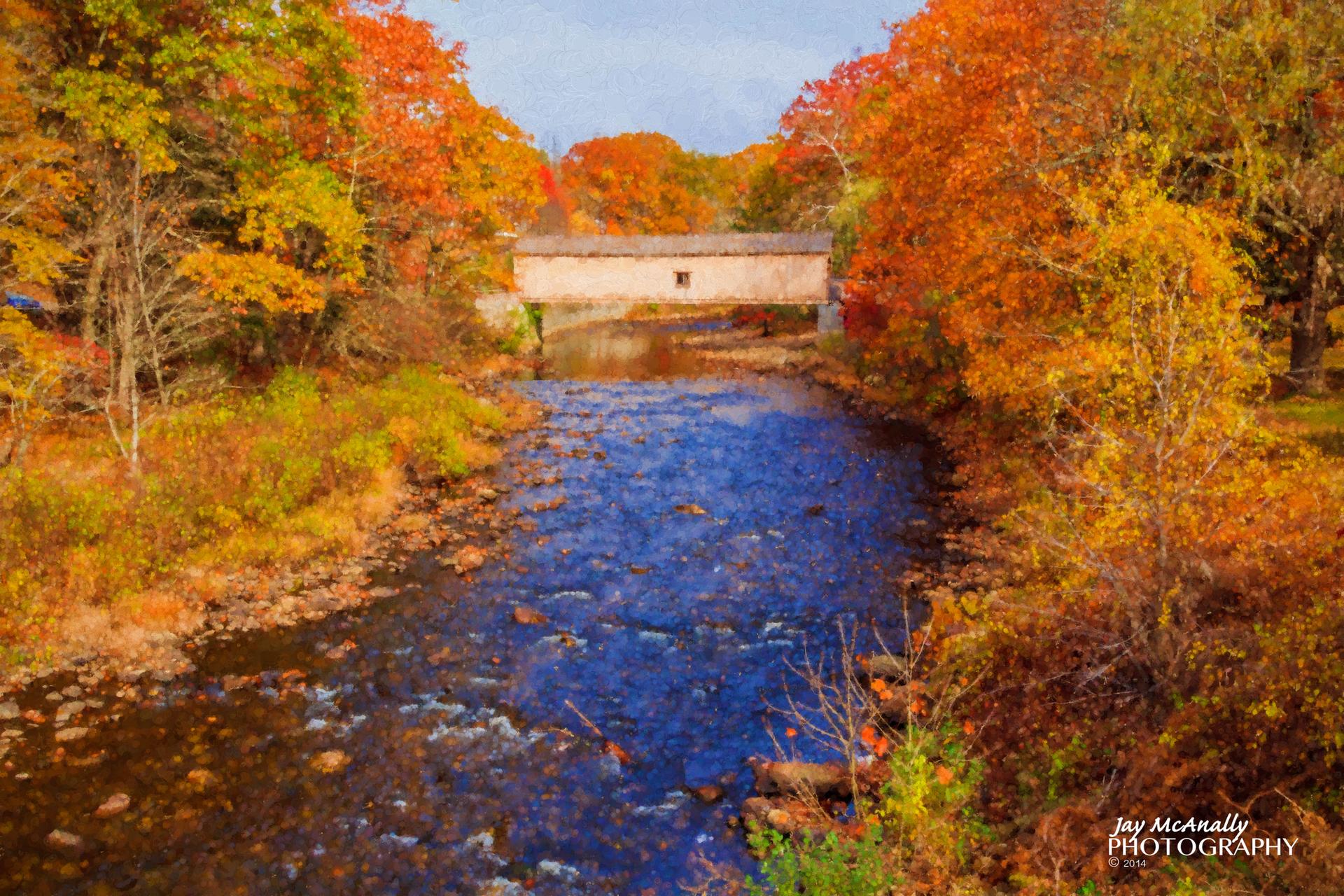Covered bridge over a river surrounded by colorful autumn trees on a bright day.