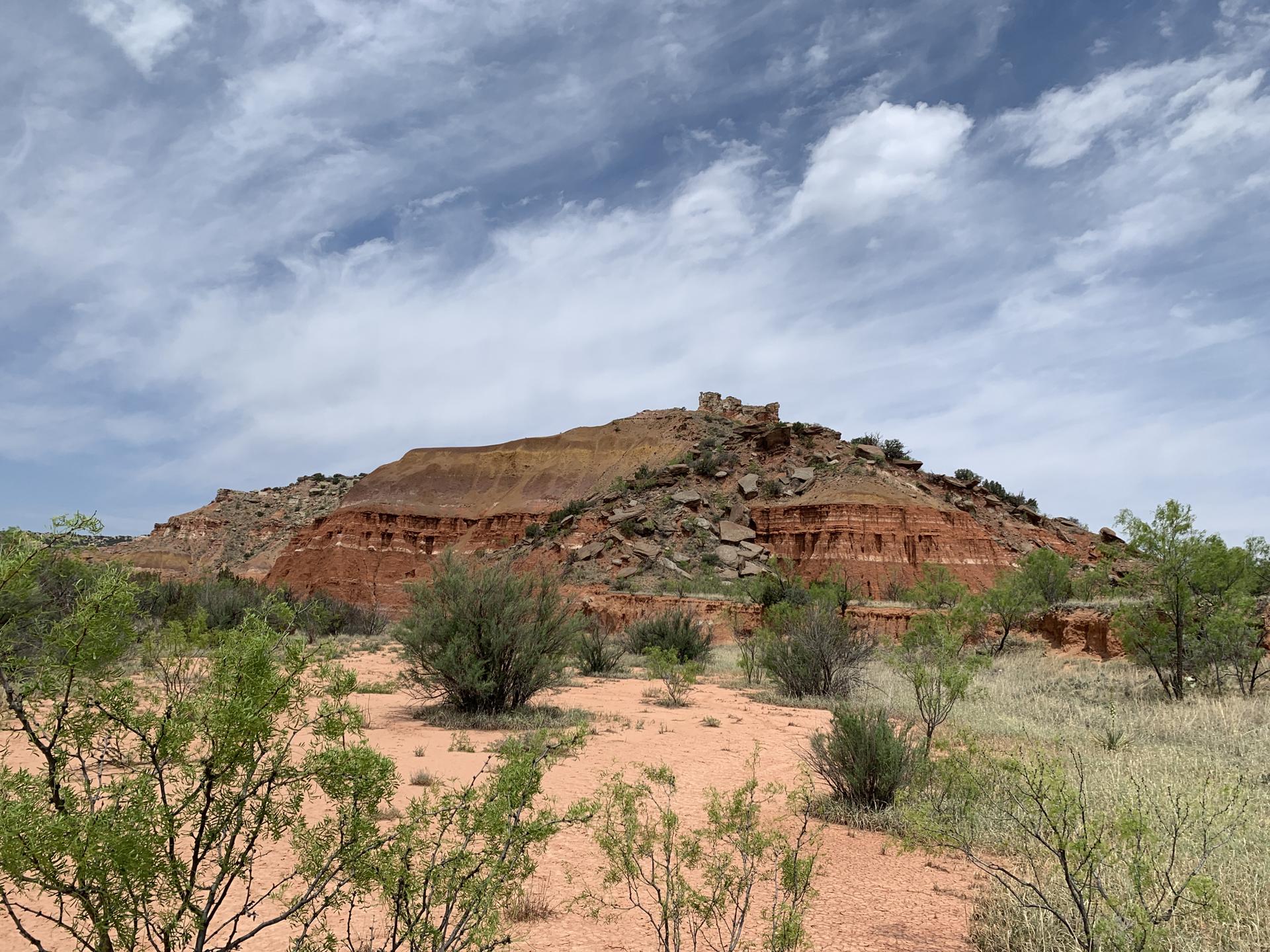 Large red mesa with sparse green bushes under a dramatic cloudy sky.