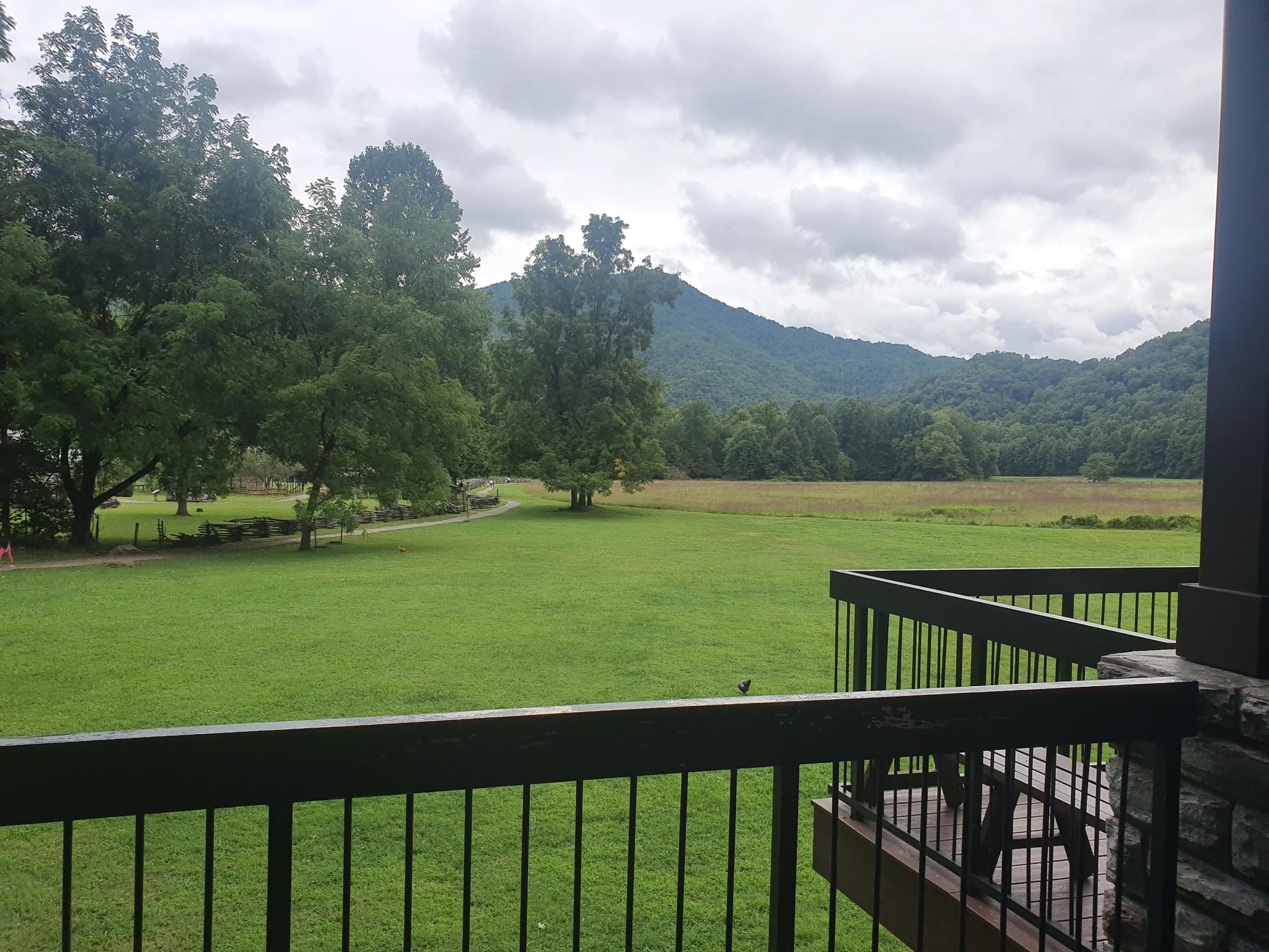 View from a balcony overlooking a vast green field and distant mountains.