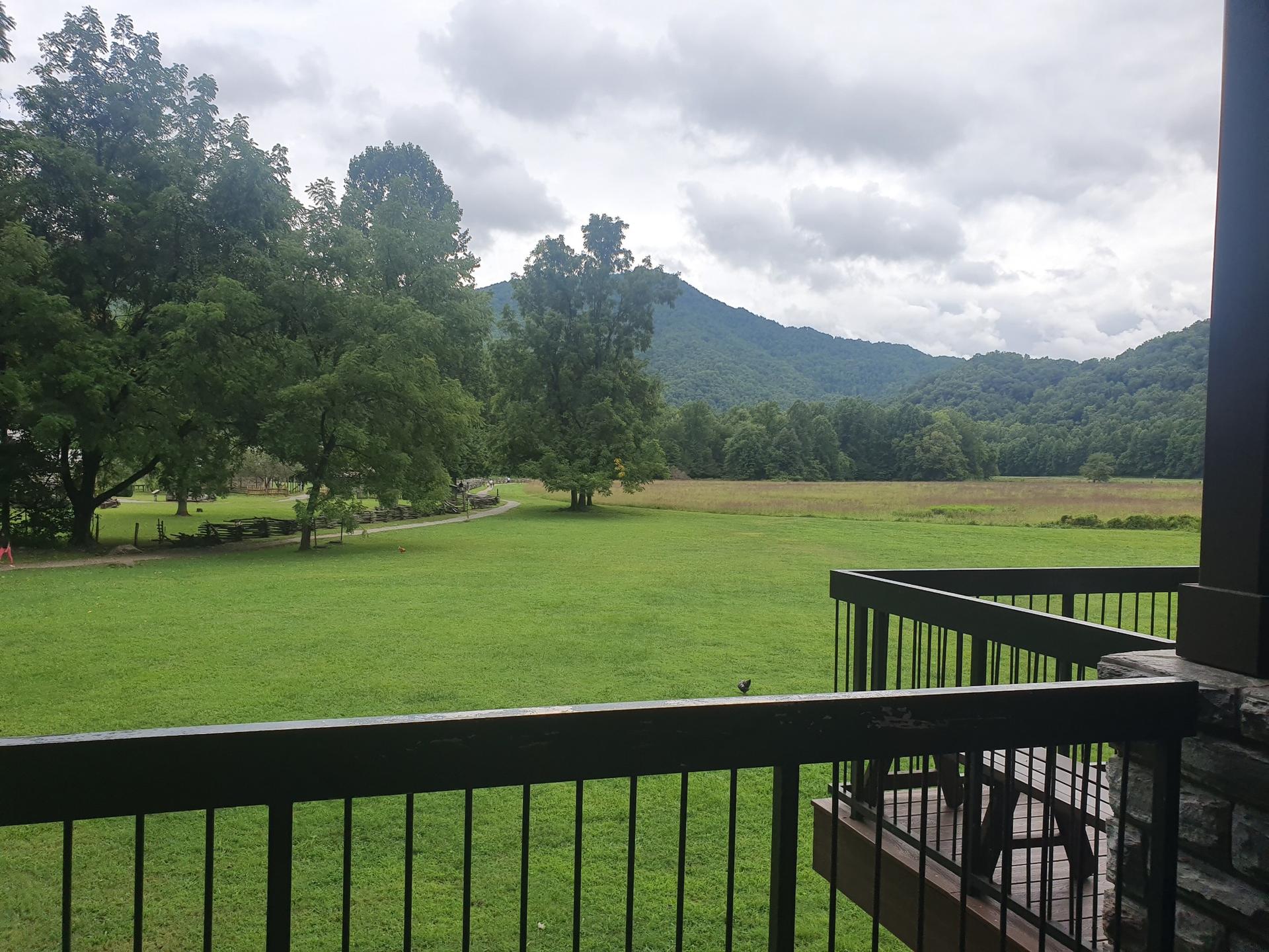 View from a balcony overlooking a vast green field and distant mountains.