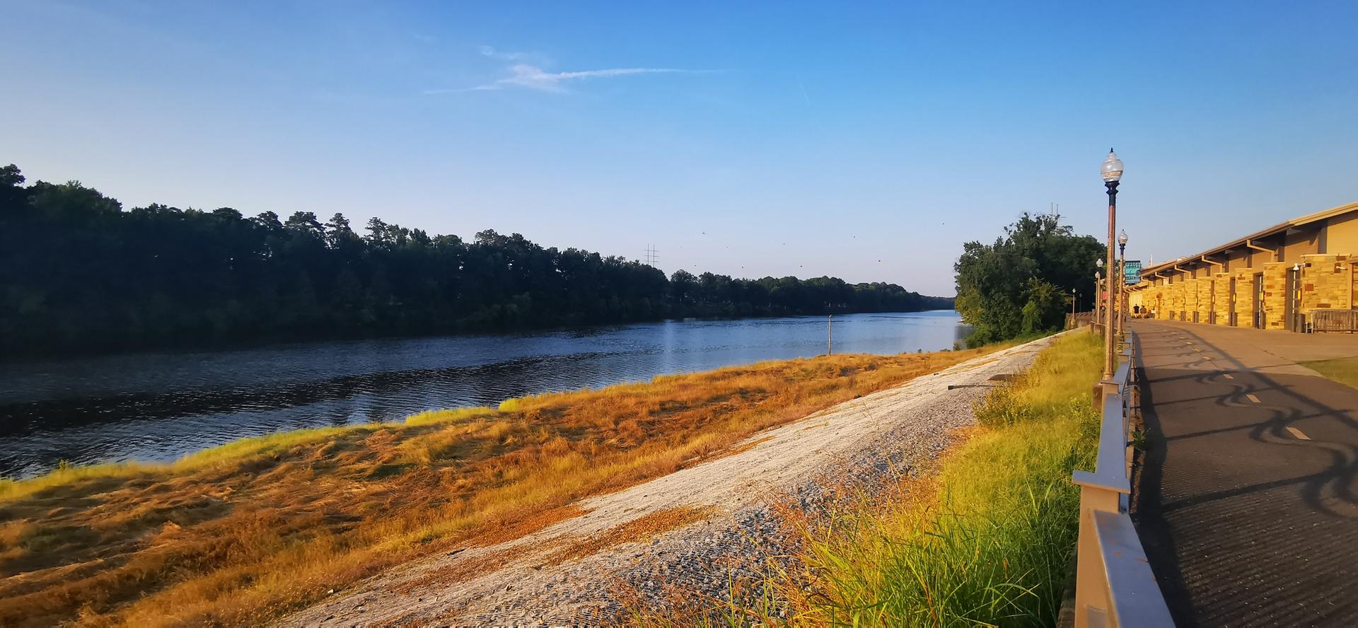 River flowing past a golden grassy embankment and urban buildings at sunrise.