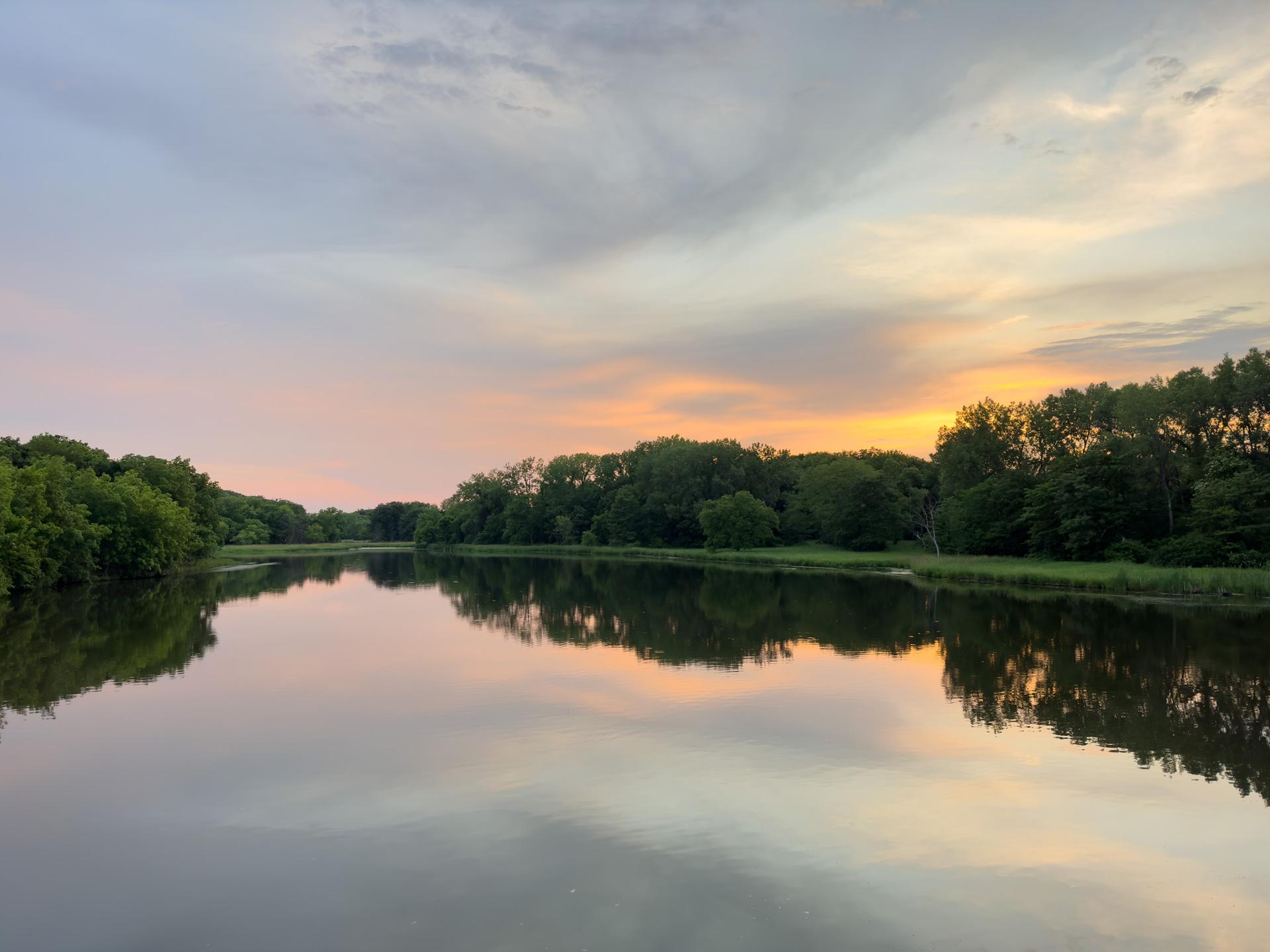 Serene lake reflecting a vibrant sunset over lush green trees.