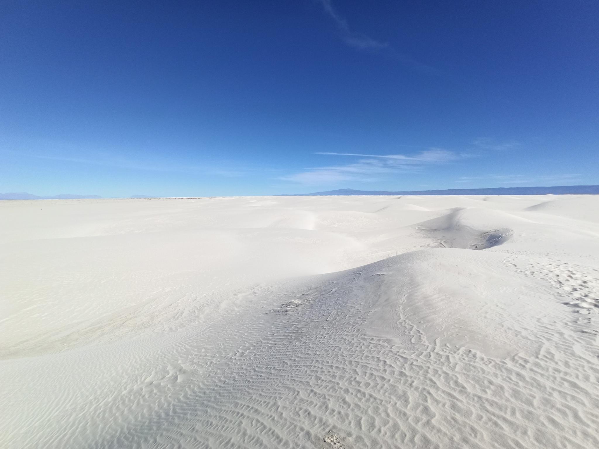 Vast white sand dunes under a clear, bright blue sky.