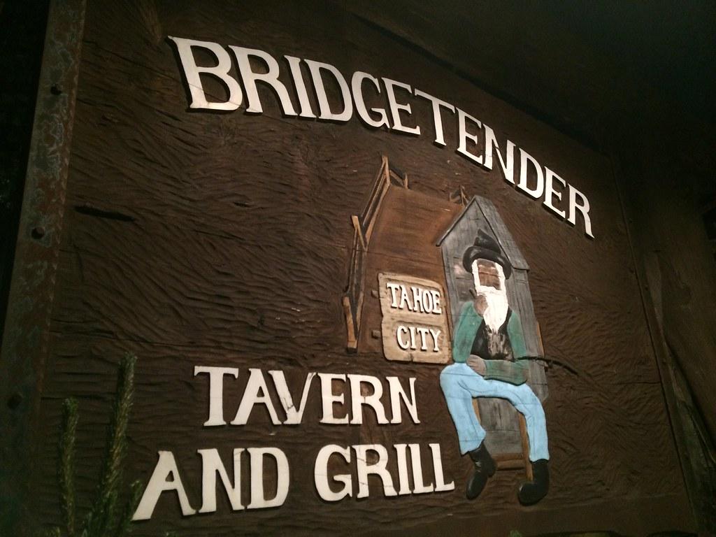 A dimly lit wooden sign for "BRIDGETENDER TAVERN AND GRILL" with a painted figure.