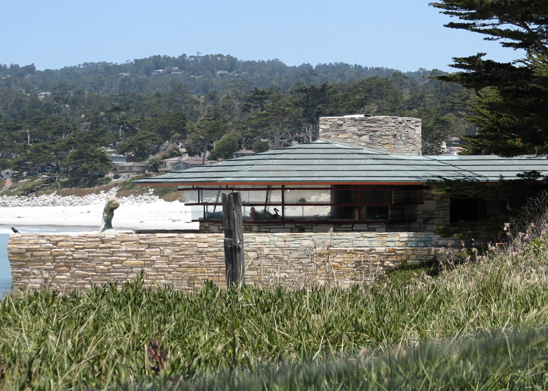 Modern stone house with a flat roof overlooking a sunny sandy beach.