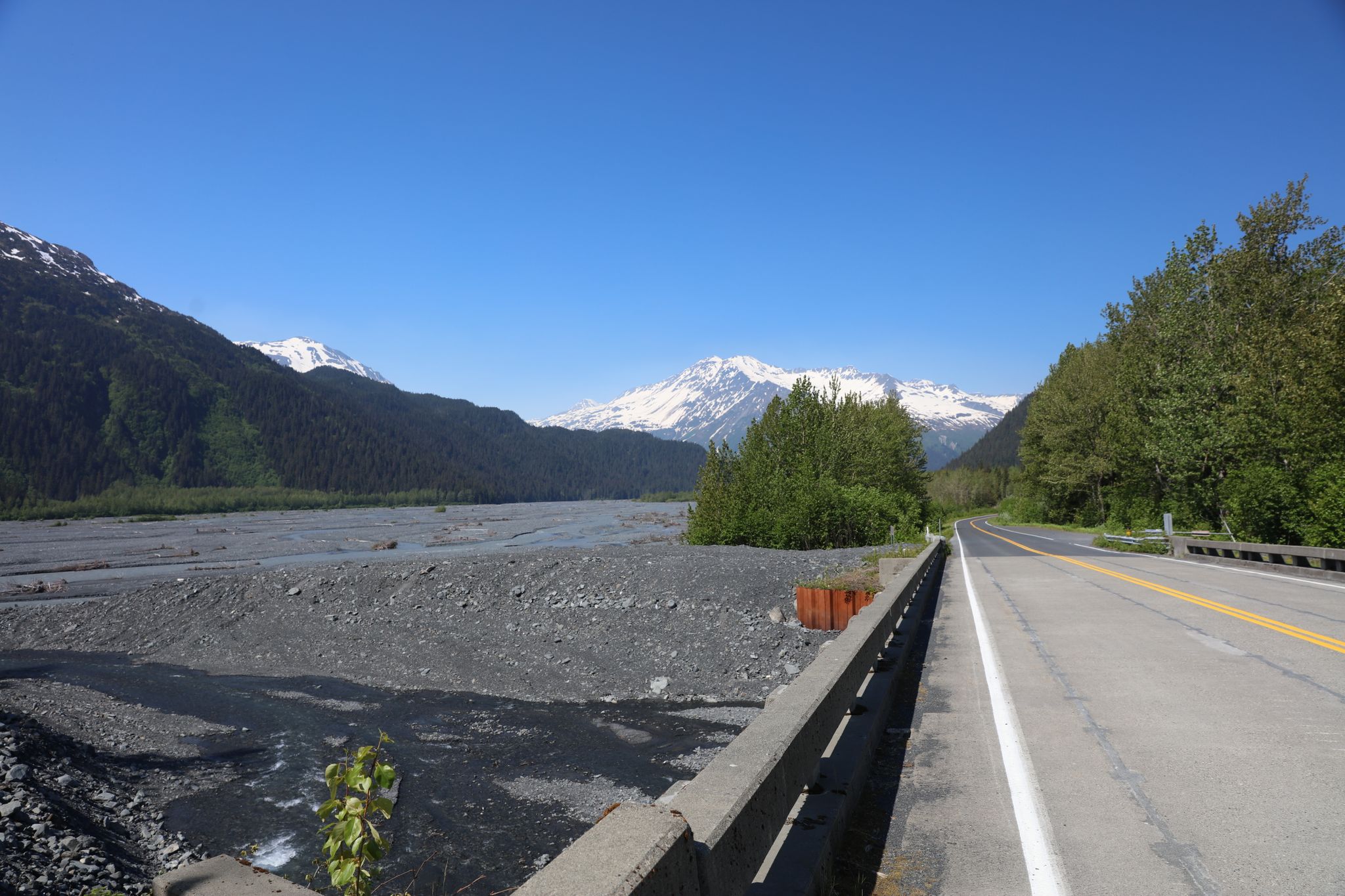 Road alongside a wide rocky riverbed with snow-capped mountains. - Seward Highway & Exit Glacier Road
