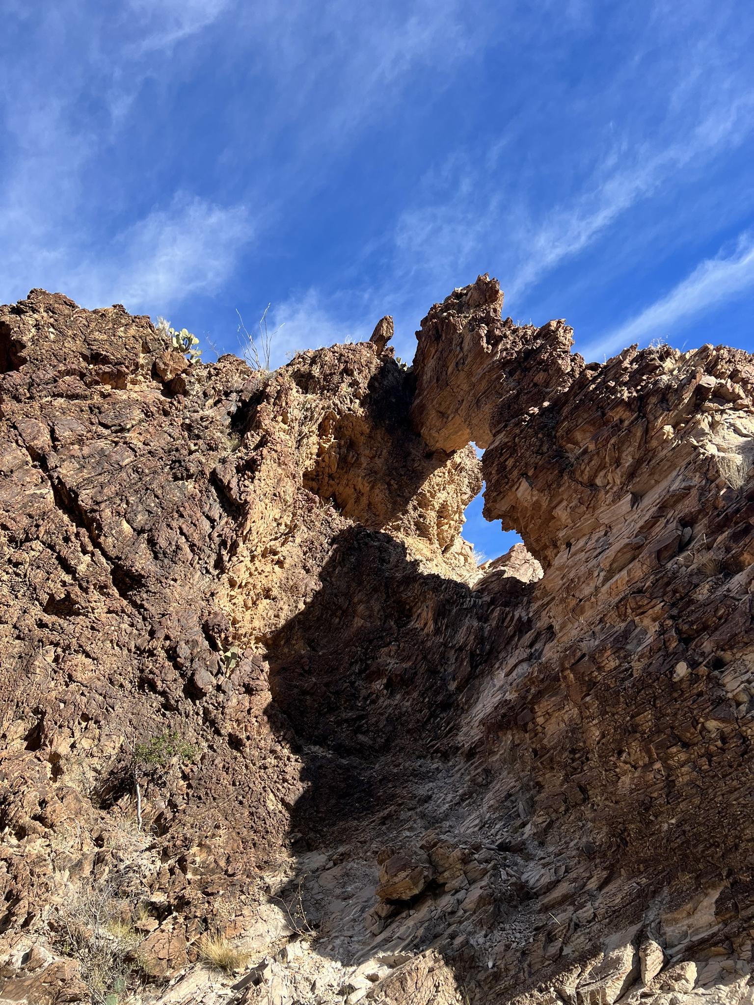 A natural rock arch frames a bright blue sky on a sunny day.