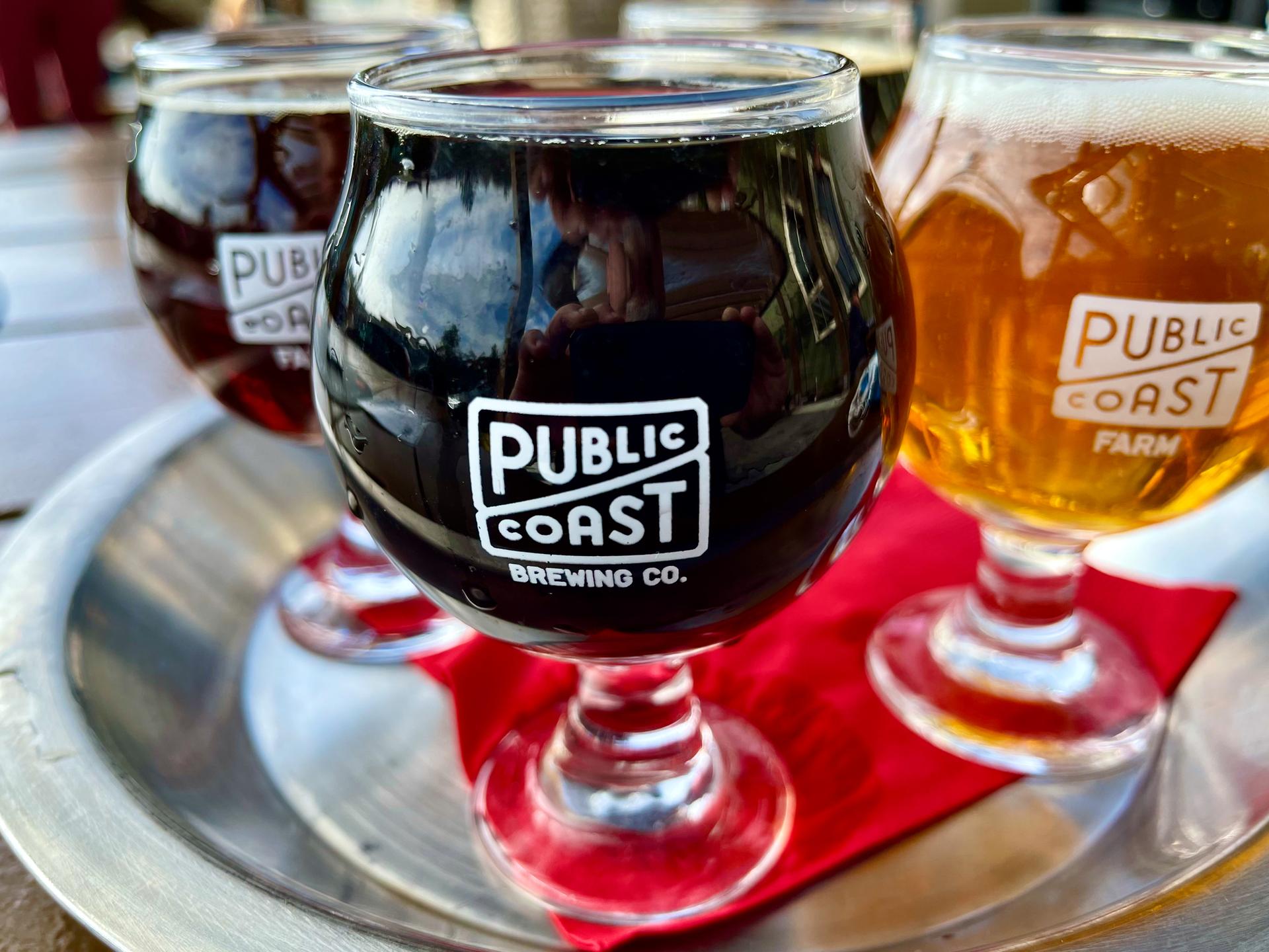 A flight of three beer glasses, two dark and one light, on a tray.