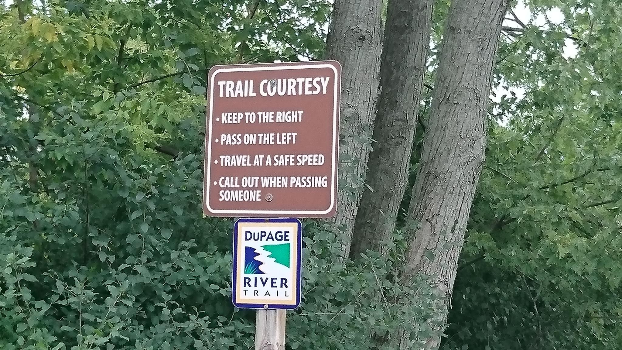 Brown trail courtesy sign and a smaller trail sign attached to a tree. - DuPage River and Southern DuPage Regional Trail Loop