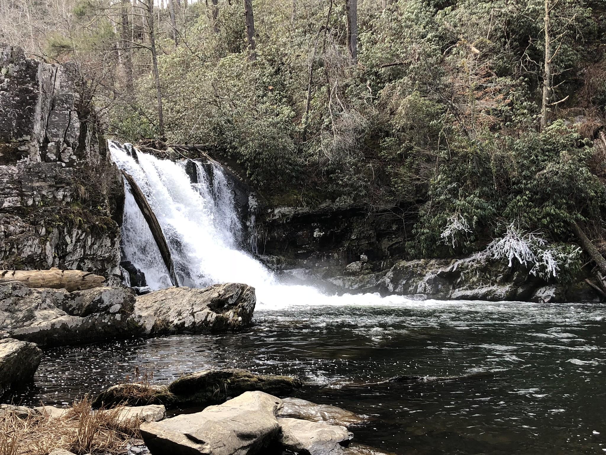 Powerful waterfall cascades into a rocky river surrounded by dense winter forest.