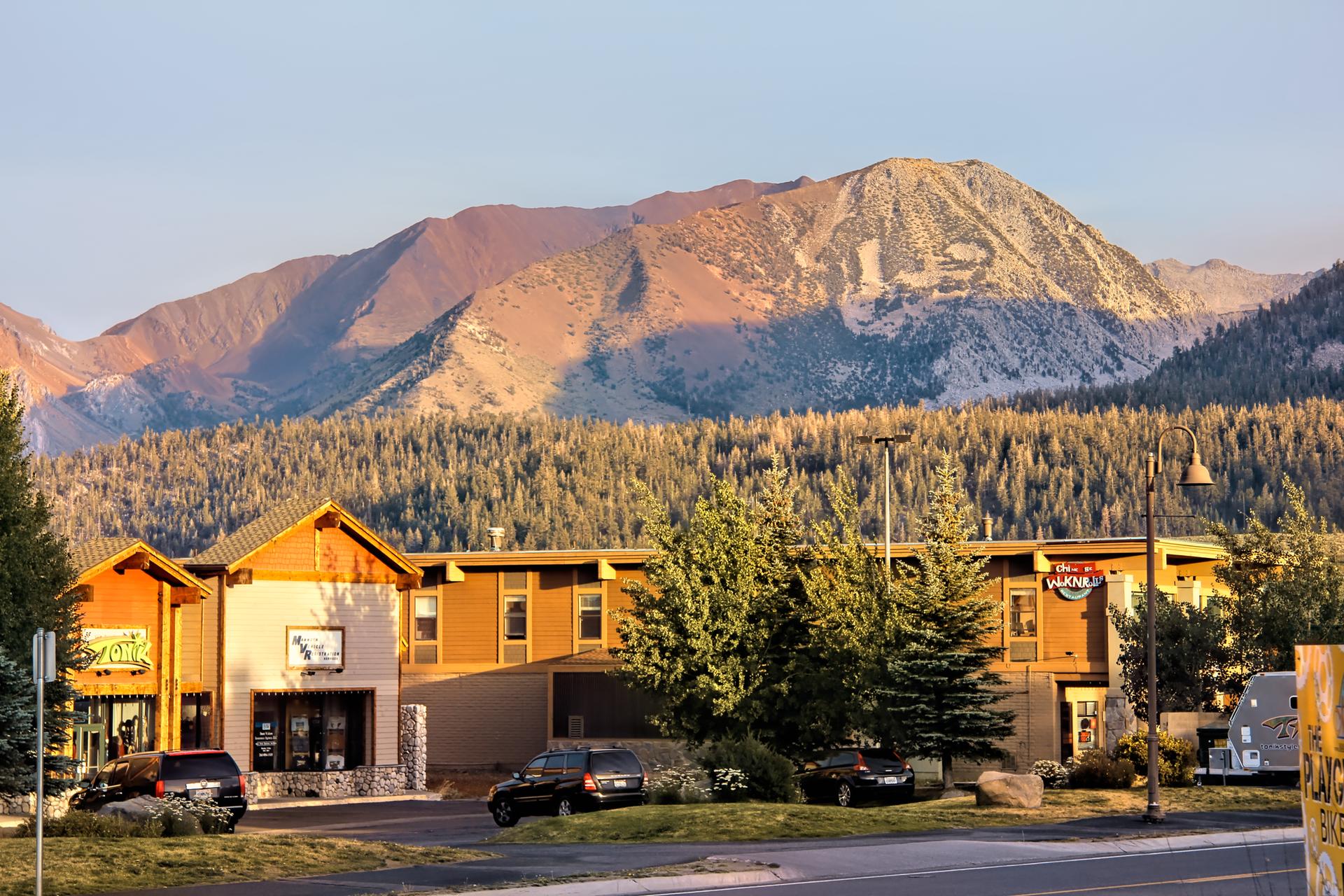 Buildings and cars at sunset with a large, rugged mountain backdrop.