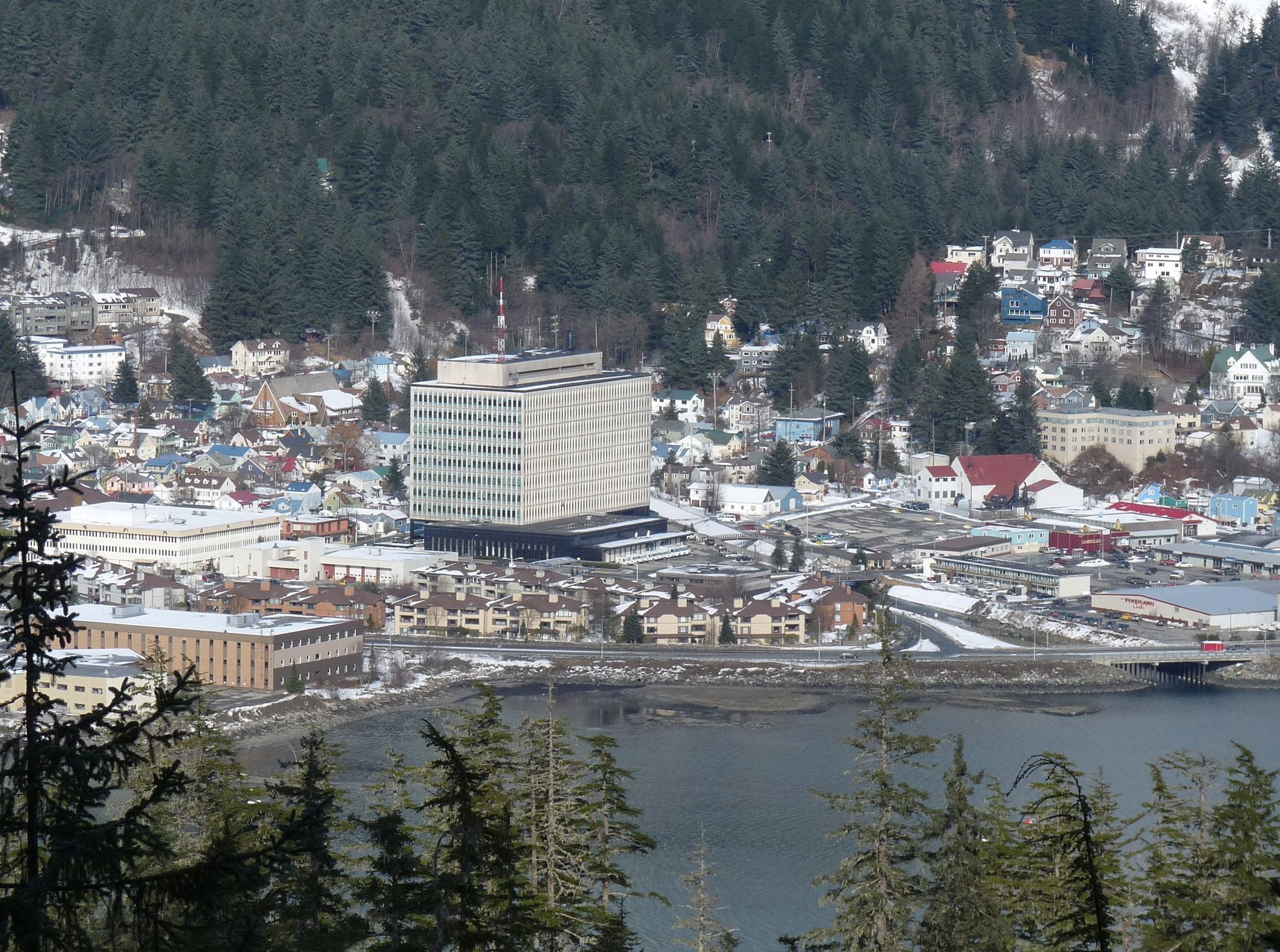 A coastal town with buildings and a large structure, backed by a snowy mountain. - Treadwell Ditch Trail