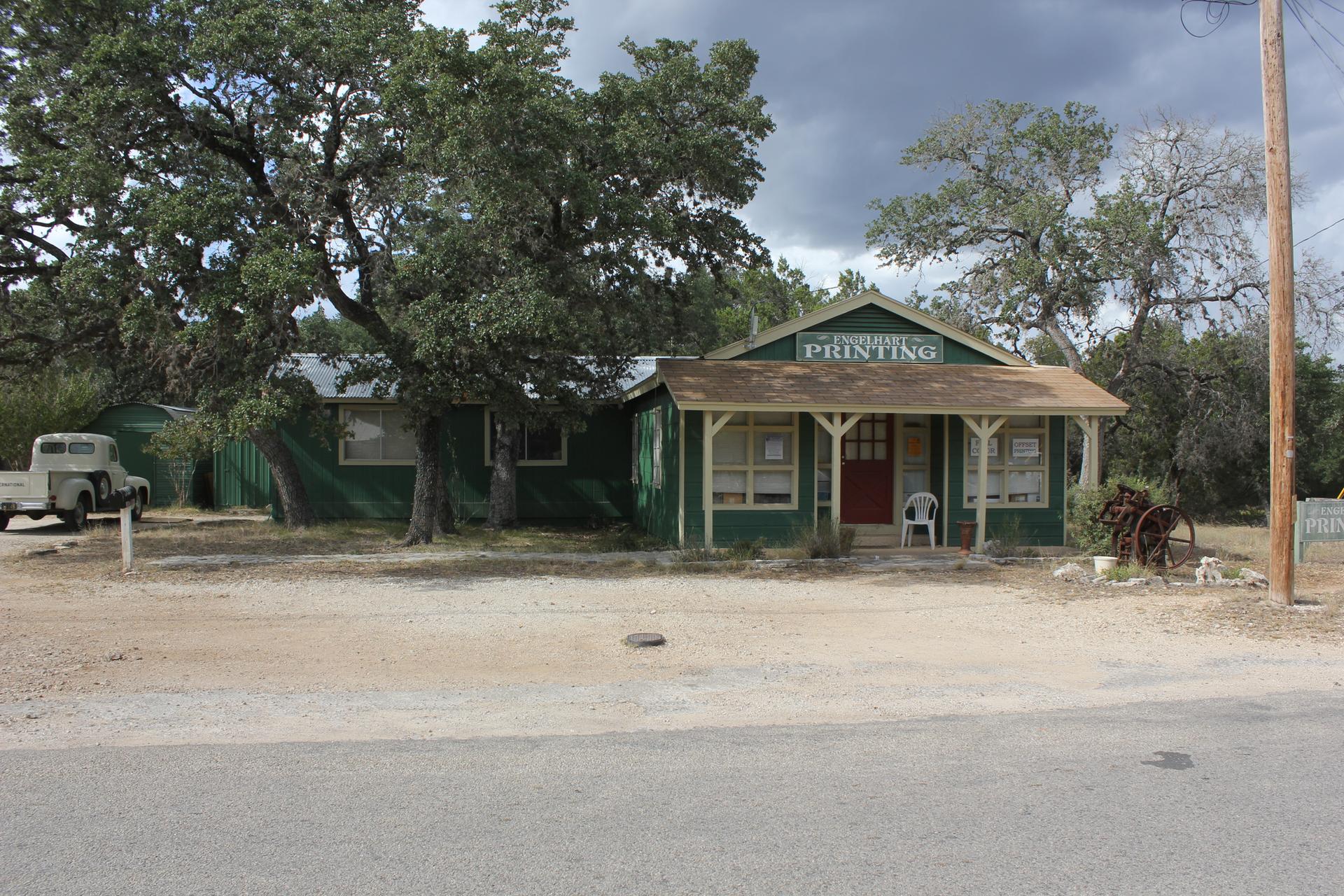 Rustic green printing shop and old truck surrounded by trees on a cloudy day.