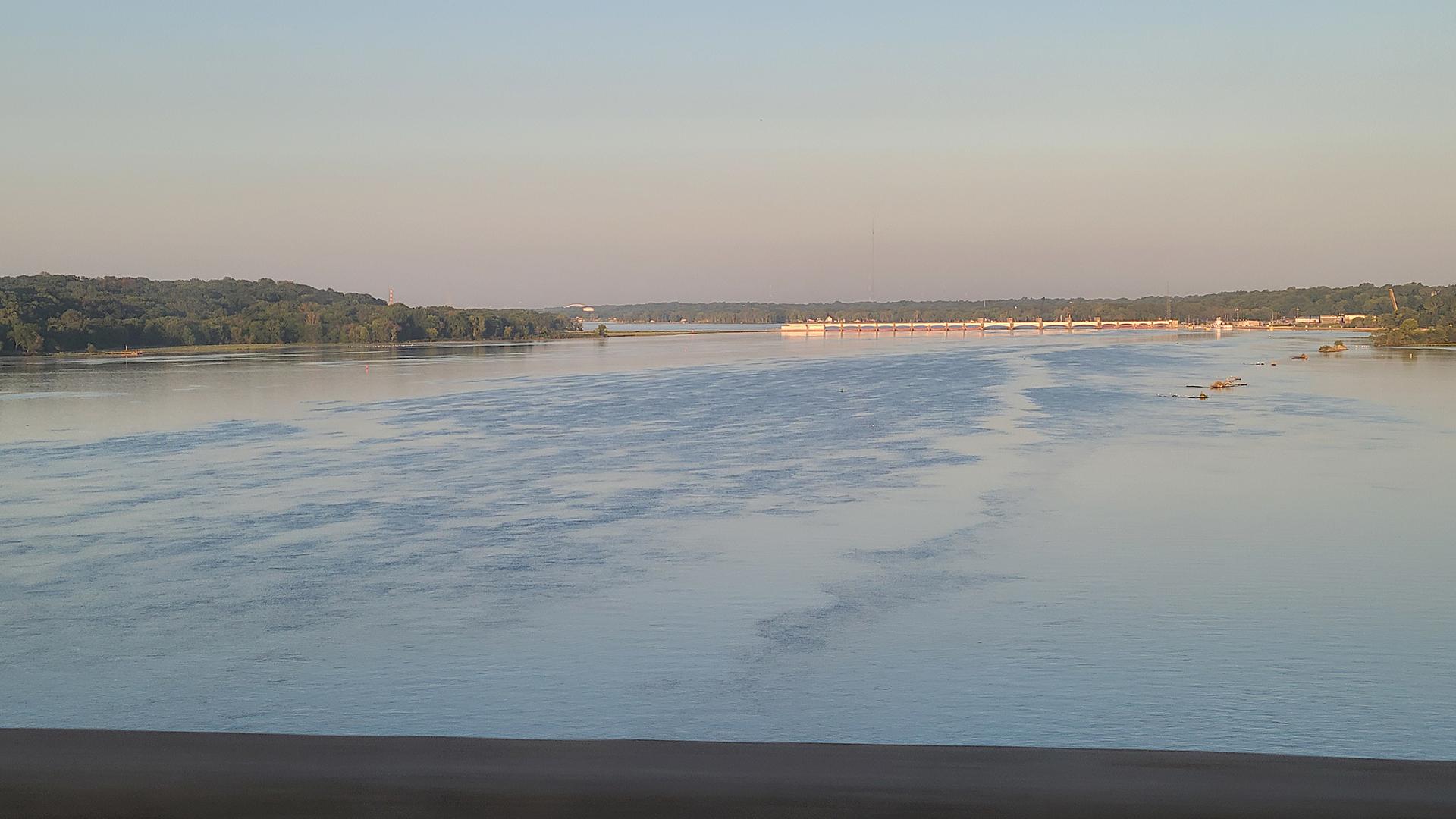 Wide river with tree-lined banks under a clear, soft sky.