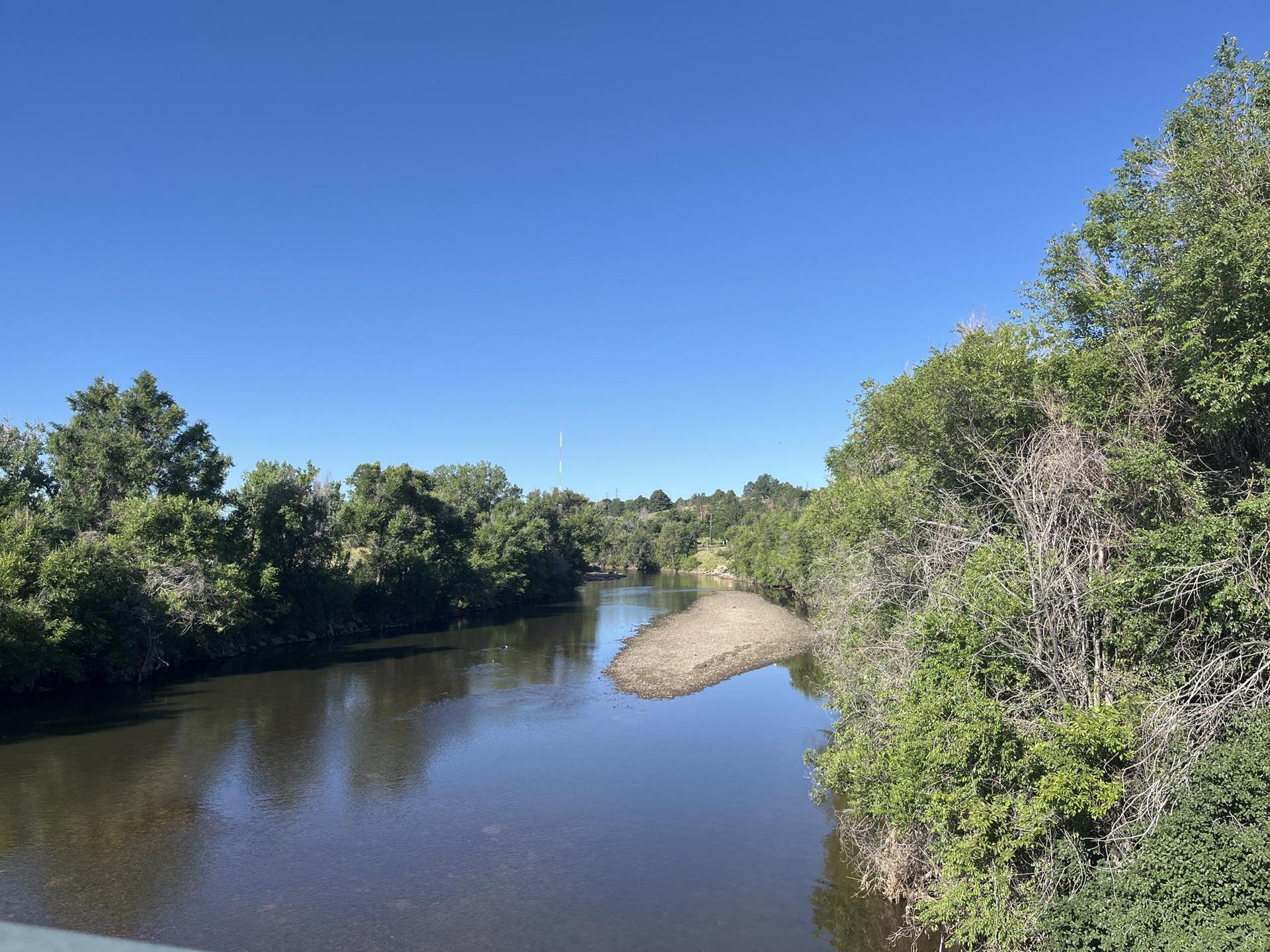A calm river winds through dense green trees under a clear blue sky.