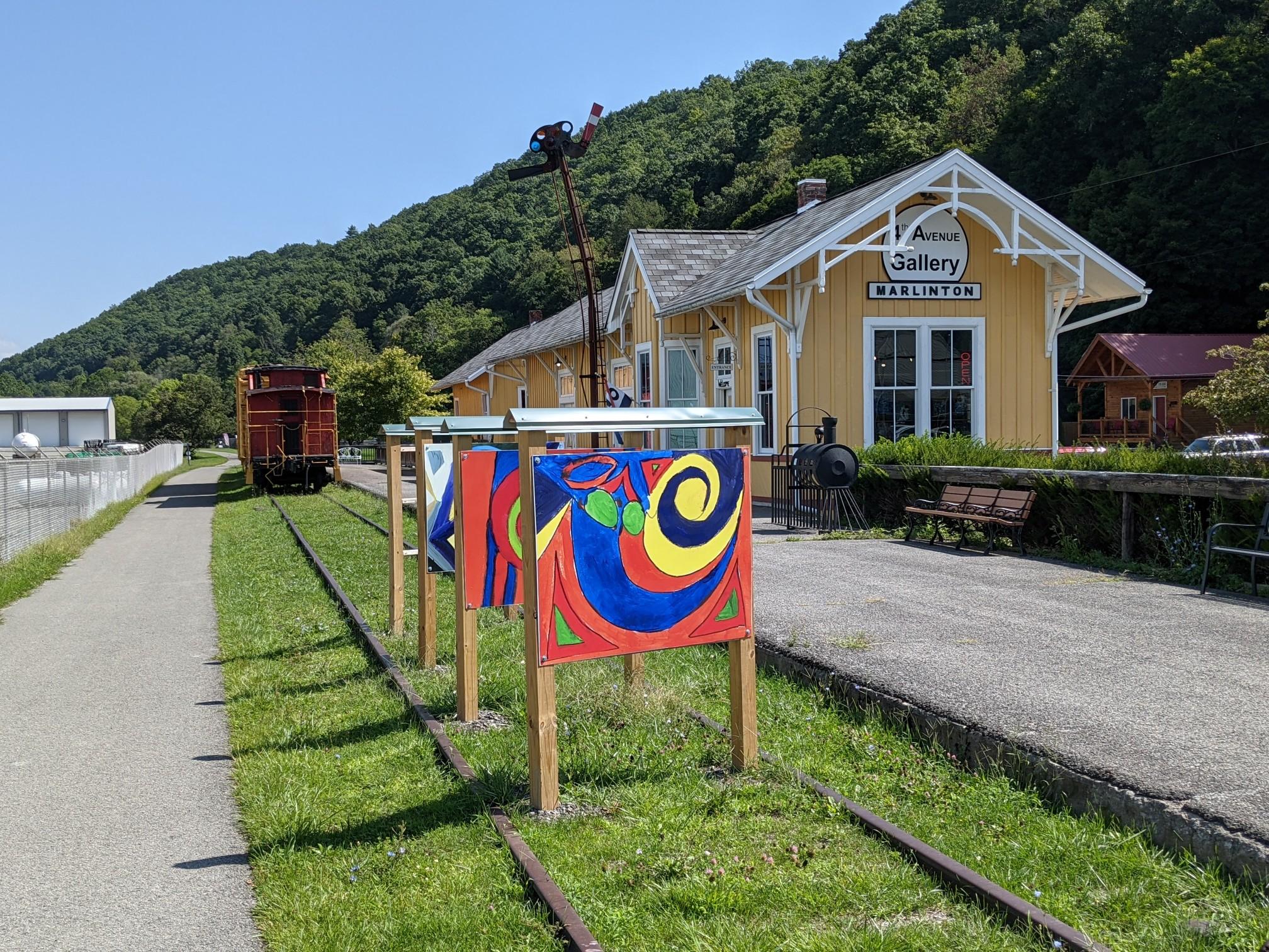 A yellow building, train car, and colorful art displays under a sunny sky.