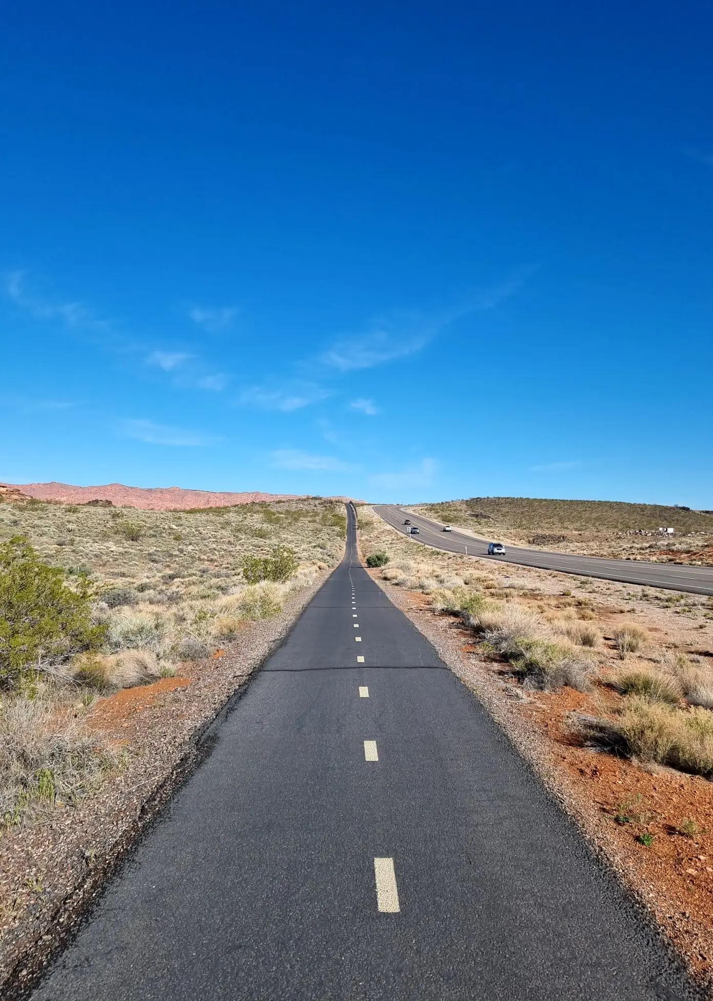 Paved path stretches through arid landscape under a bright blue sky.