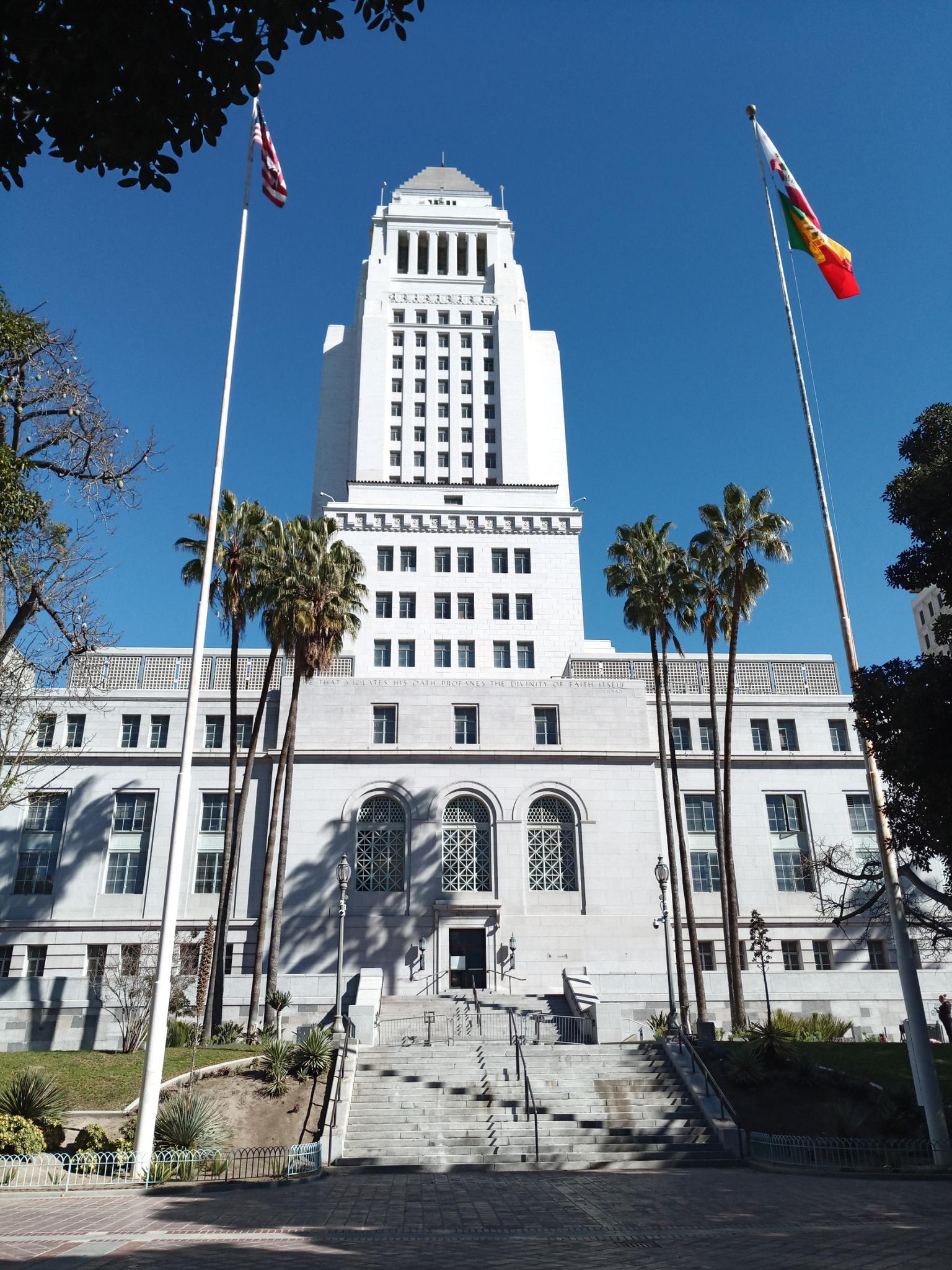 Grand white building with a tall tower, flags, and palm trees under blue sky.