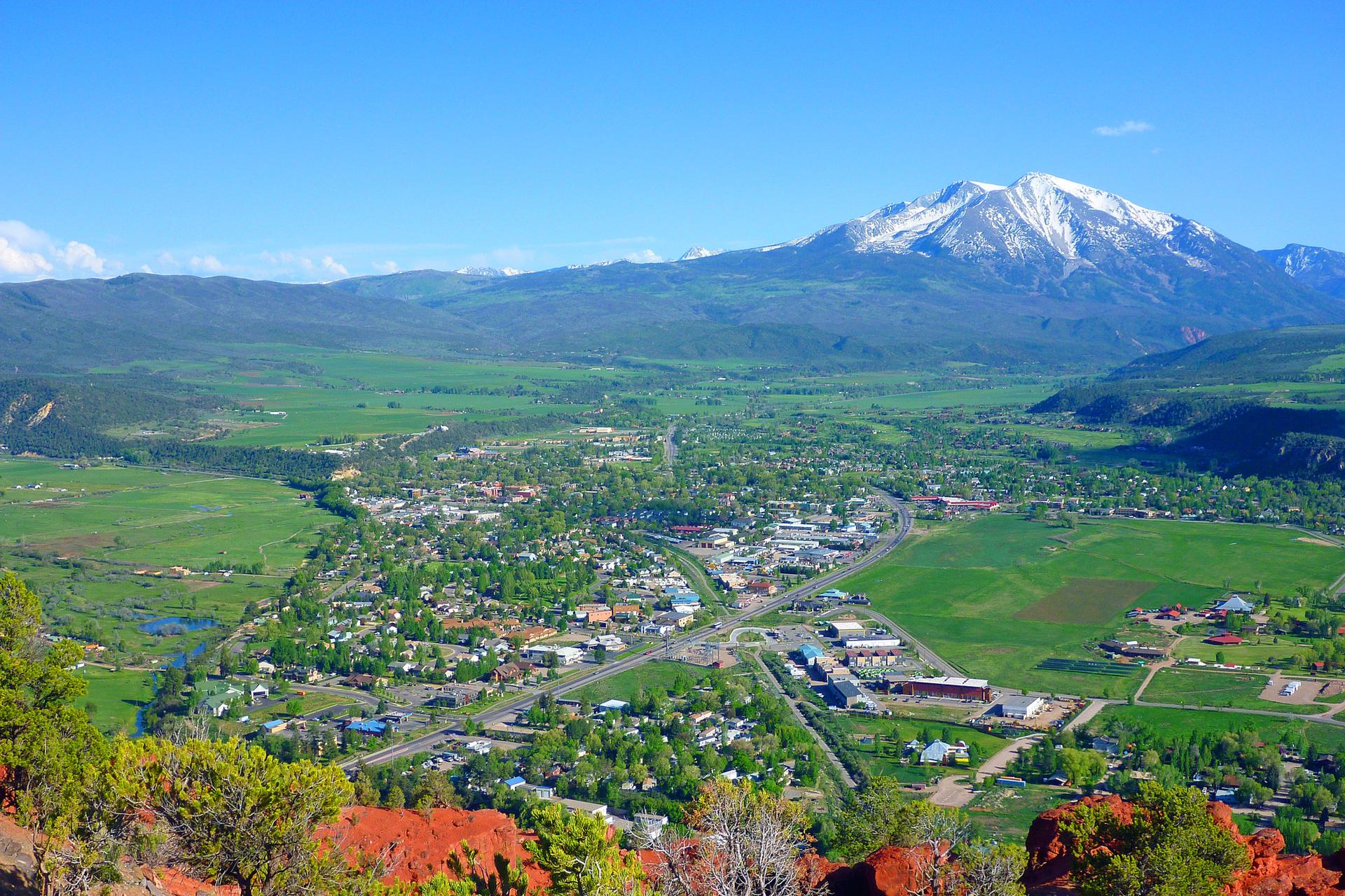 Panoramic view of a town in a green valley, with a snow-capped mountain.