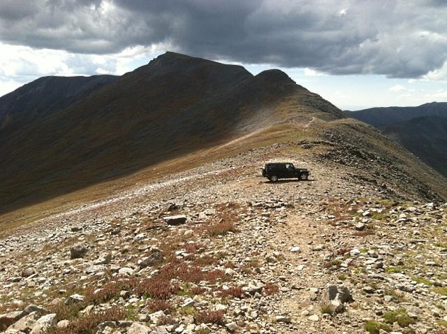 Dark SUV on a rocky mountain ridge under a cloudy sky.