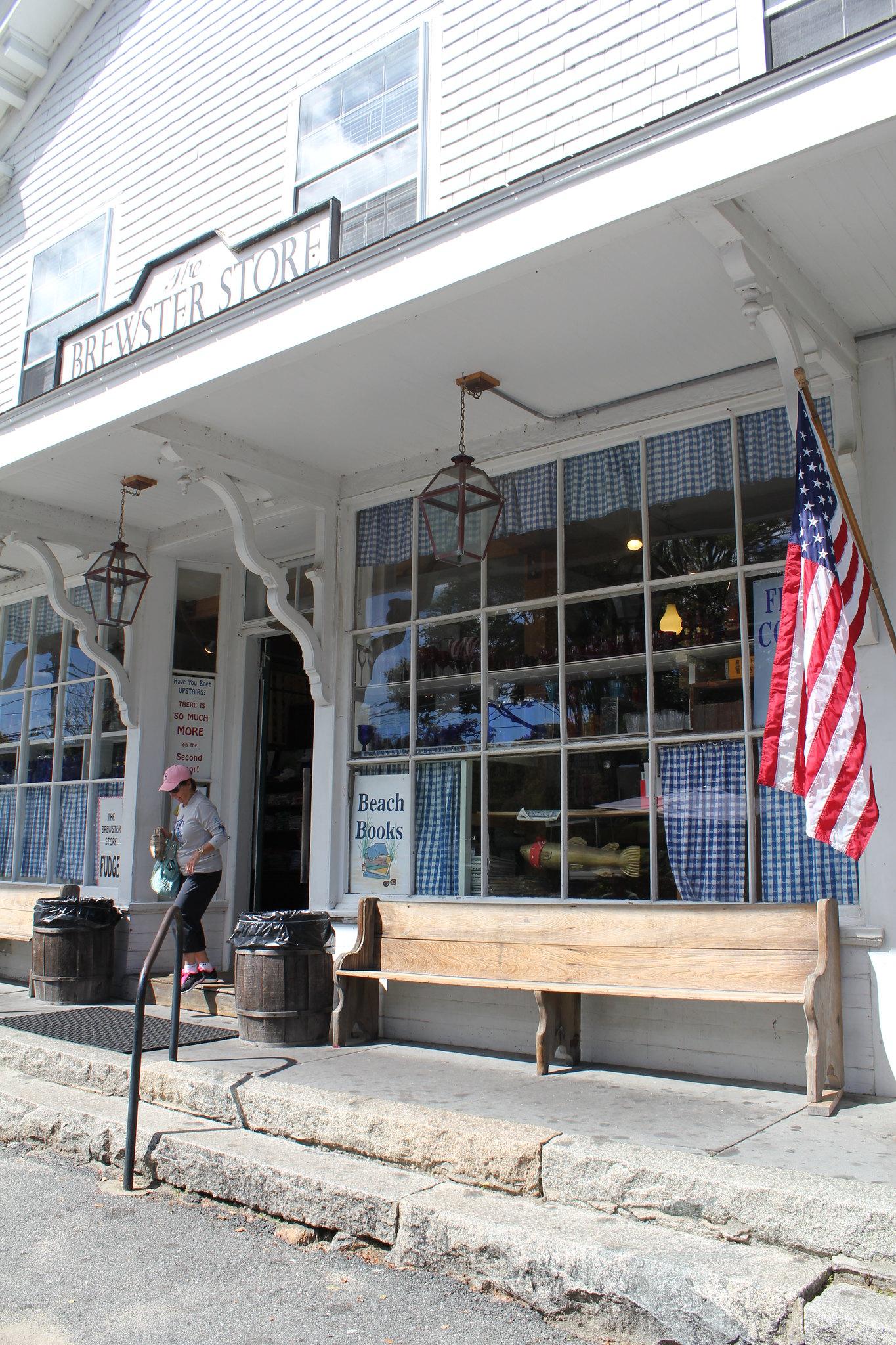 A white store building with an American flag and a person exiting on a sunny day.