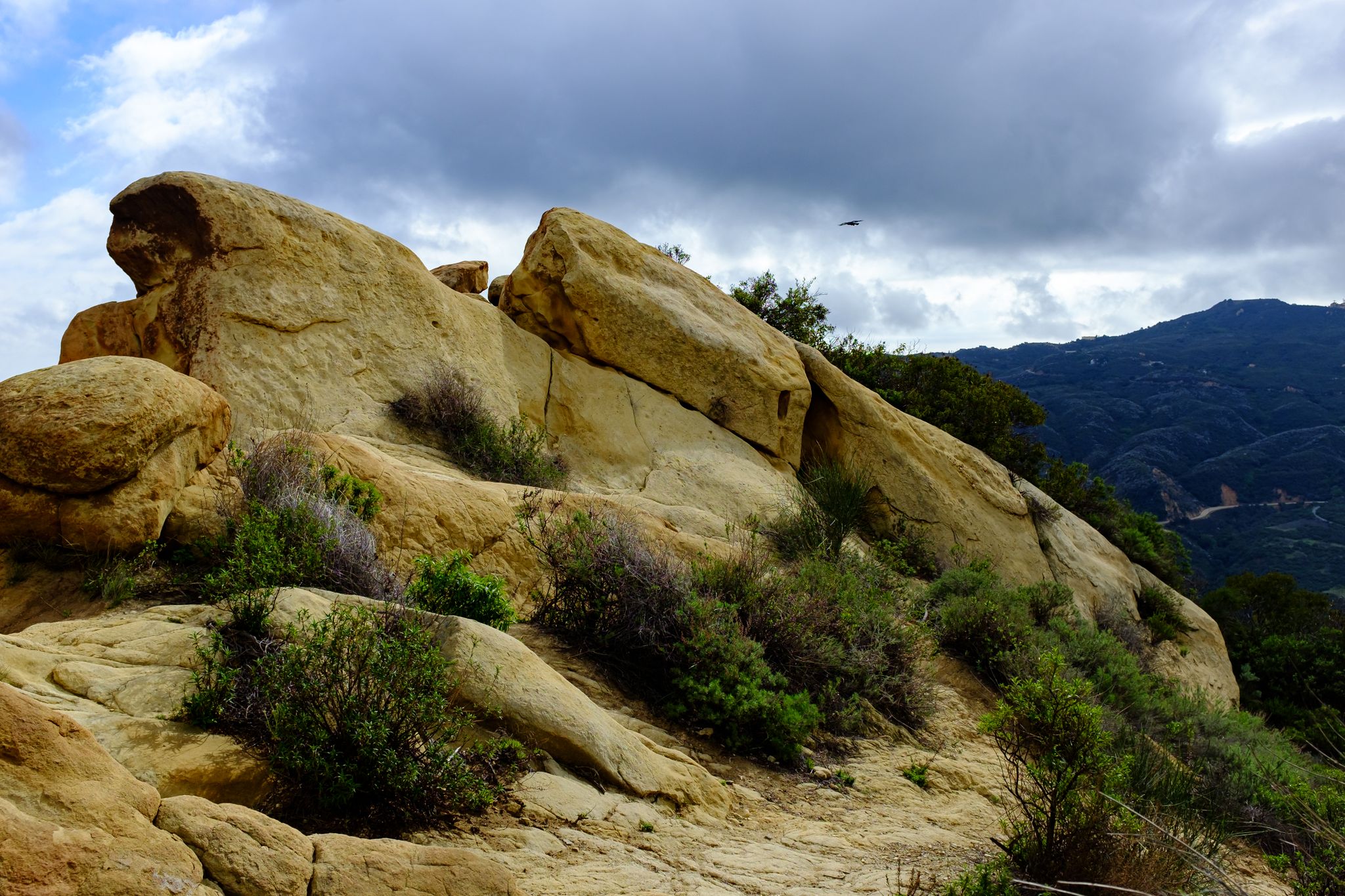 Large rock formations and scrub brush under a cloudy sky with distant mountains. - Calabasas Peak and Secret Valley Loop