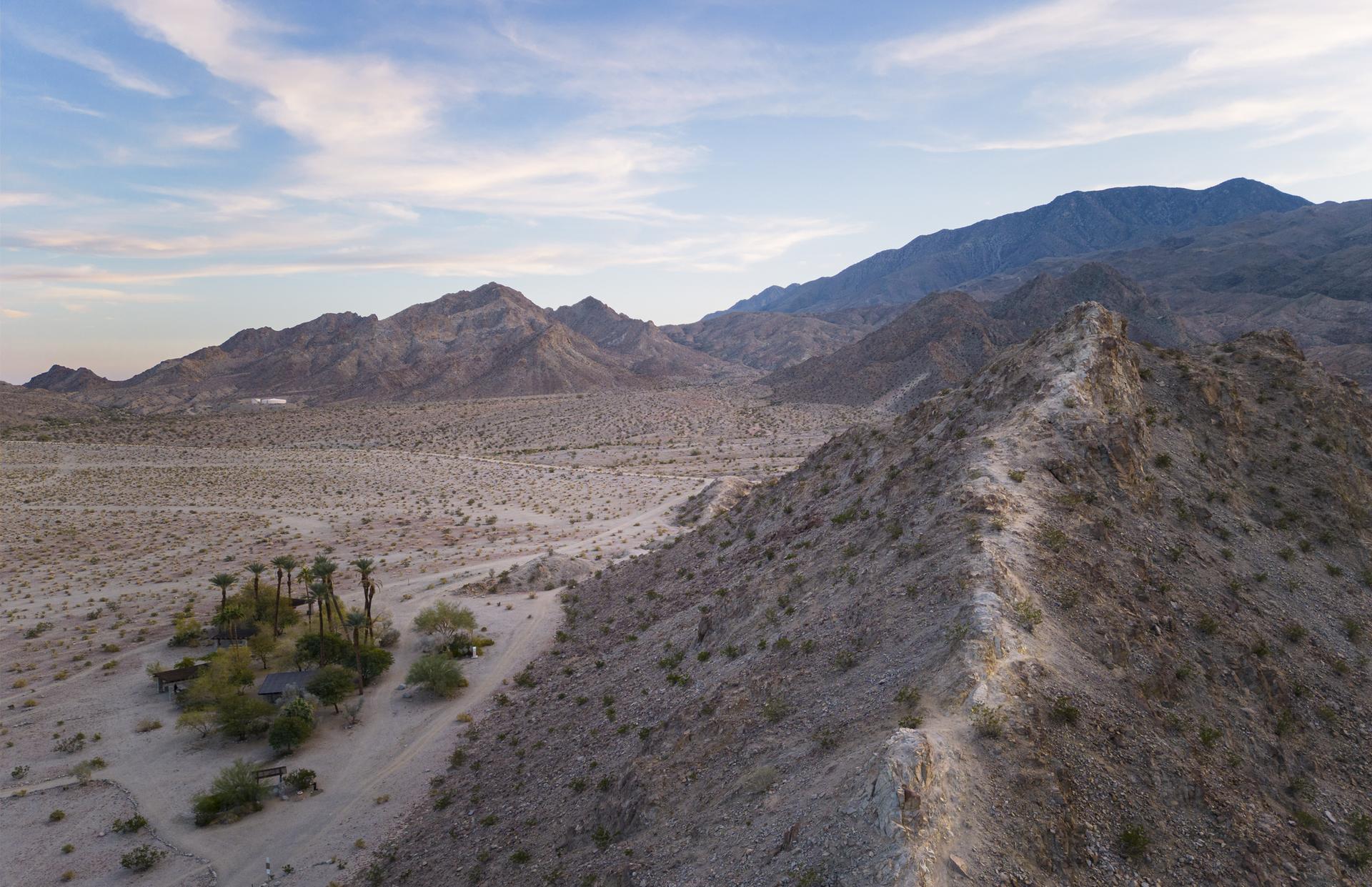 Aerial view of a vast desert with rugged mountains and a small green oasis.