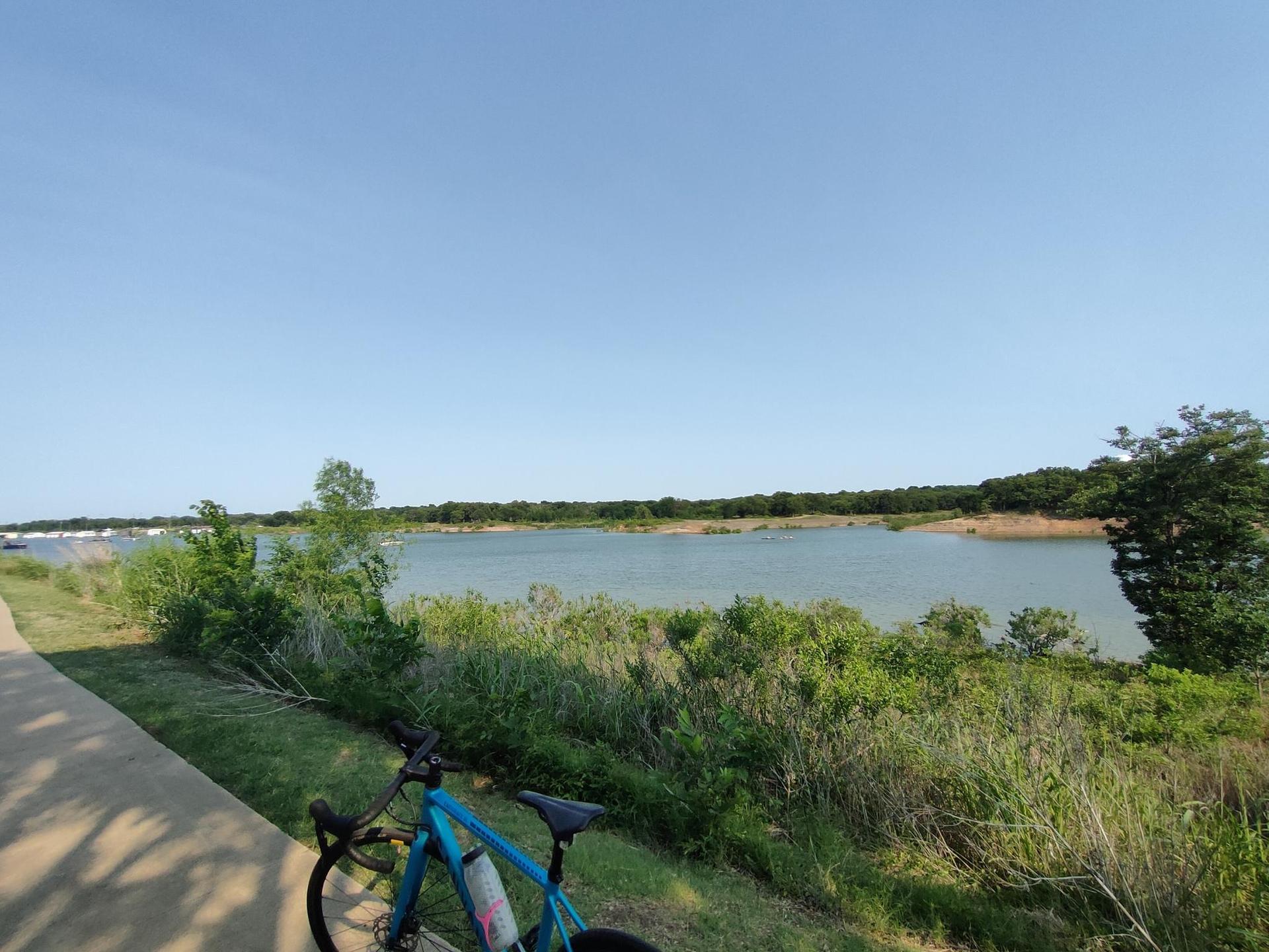 Blue bicycle on a sunny paved path overlooking a lake and green trees.
