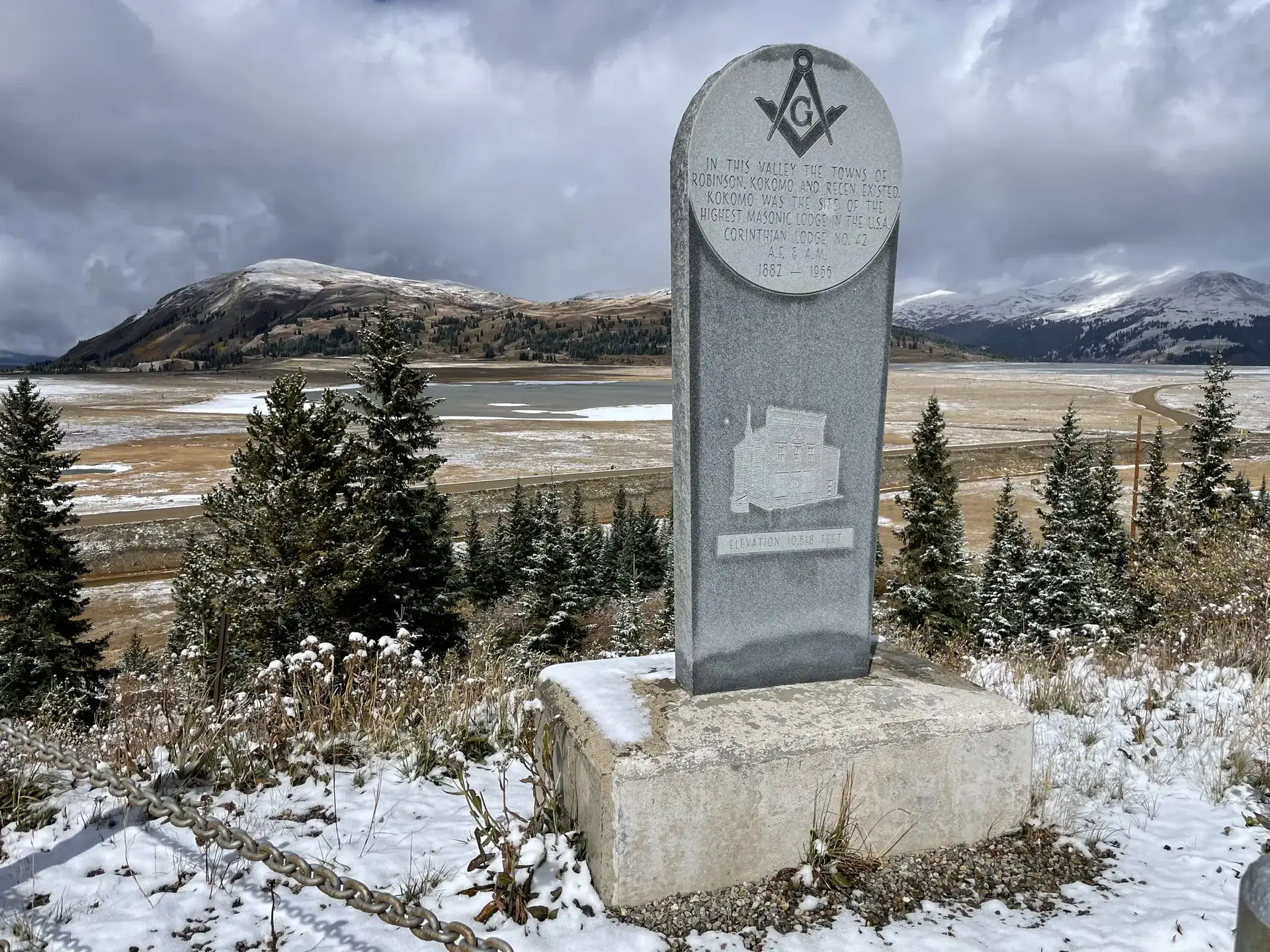 Stone monument in a snowy, overcast landscape with distant hills and lake.