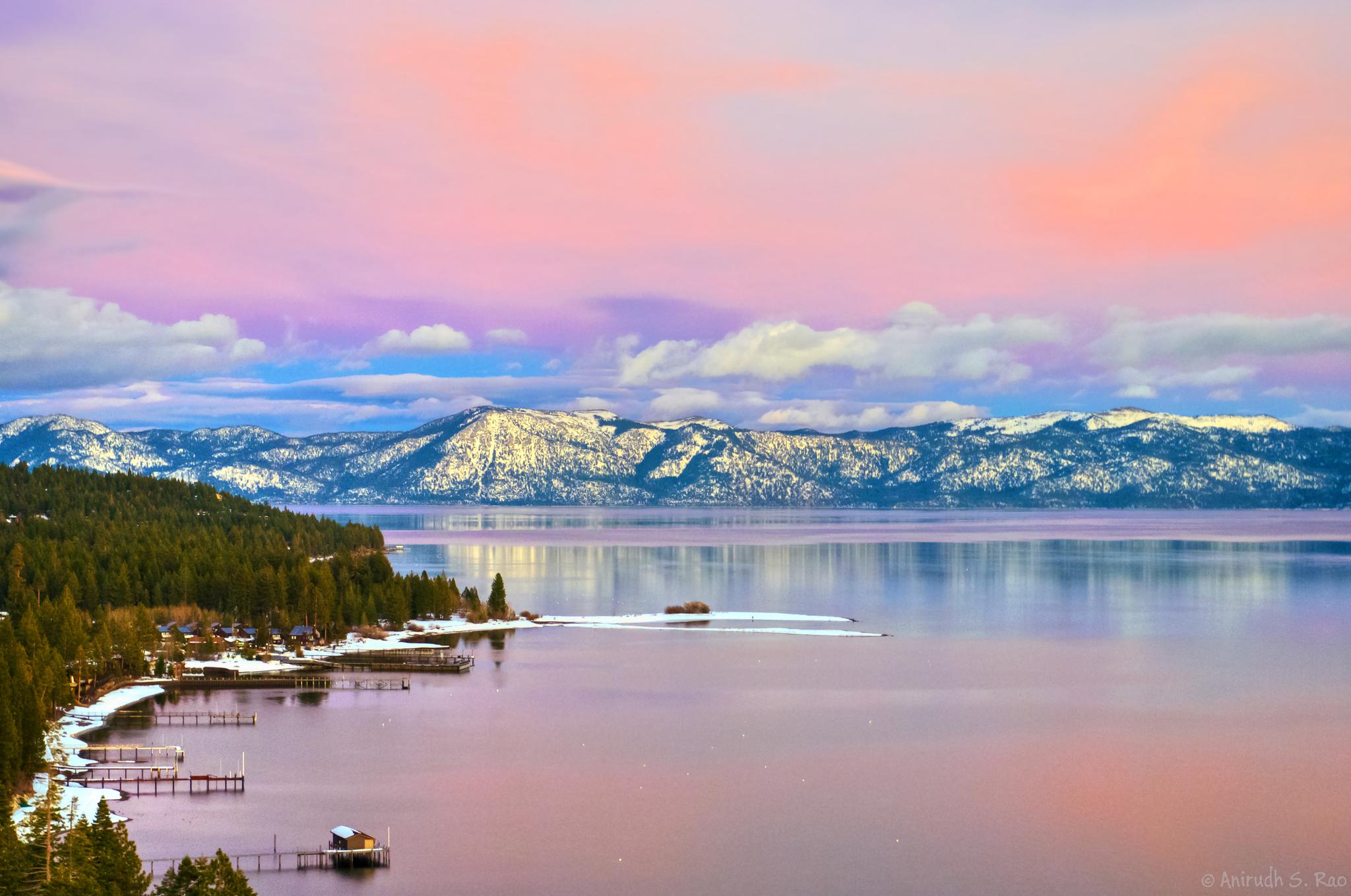 Vibrant pink and purple sunset over a large lake with snow-capped mountains.