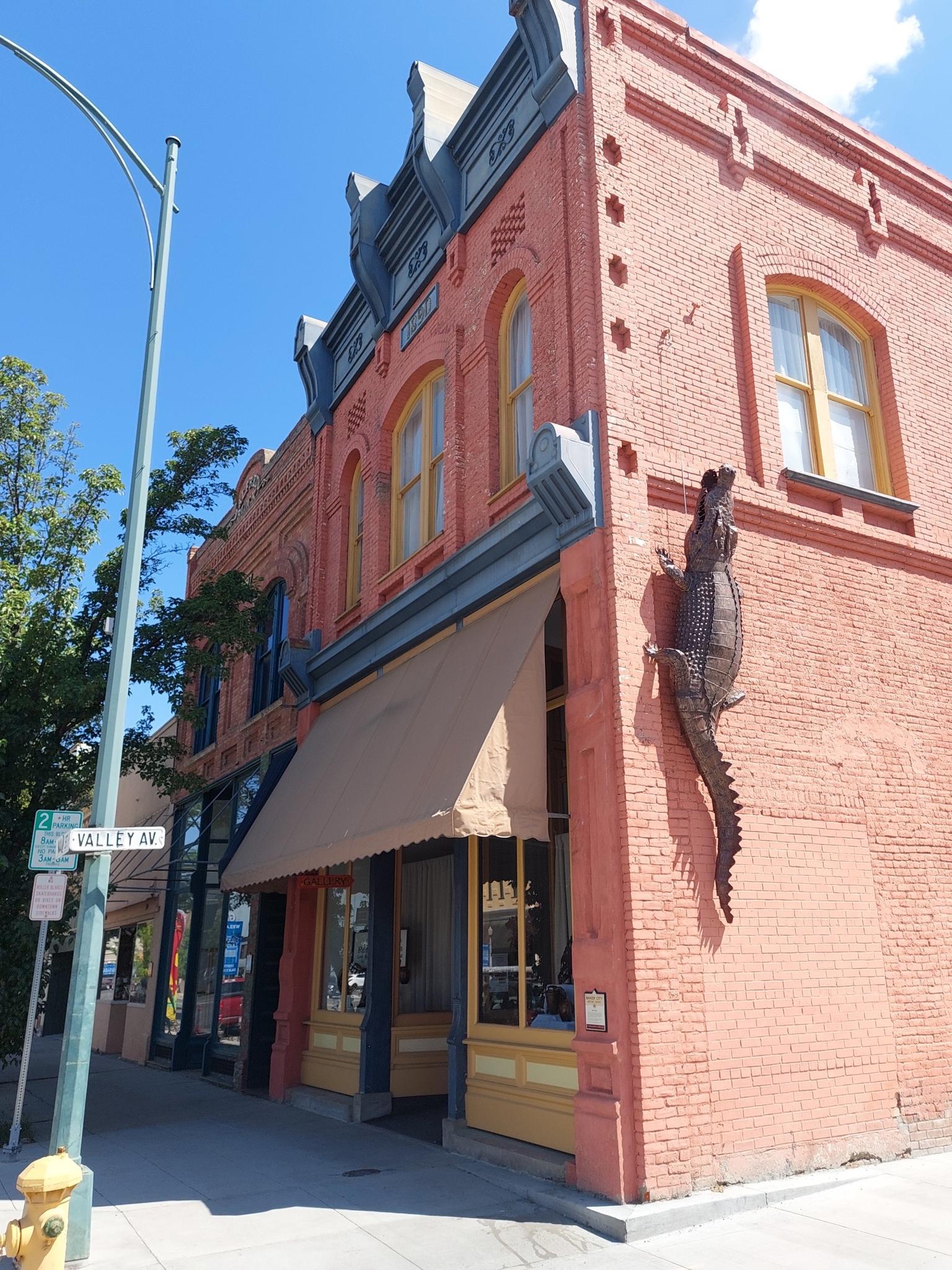 A brick building with an alligator sculpture on its side, sunny street scene.