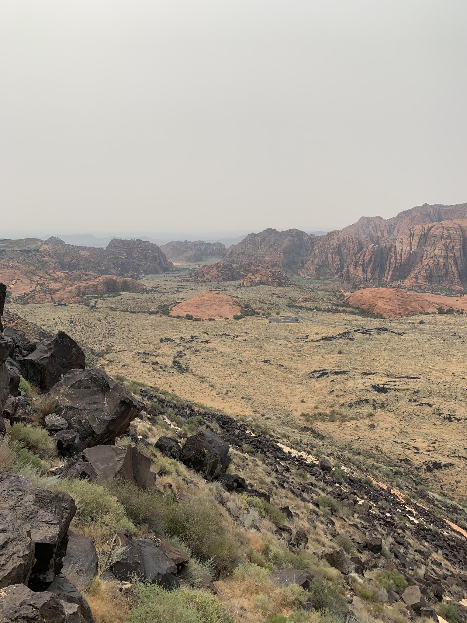 Overcast desert vista with rocky foreground, valley, and distant red rock formations.