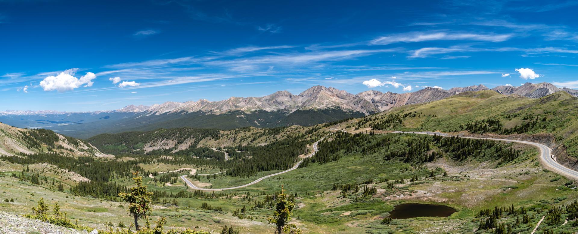 Panoramic view of a winding mountain road through green valleys under a blue sky.