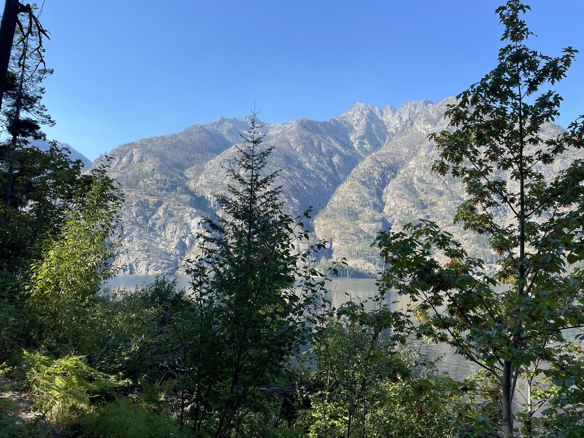 Majestic mountains rise above green trees under a clear blue sky.