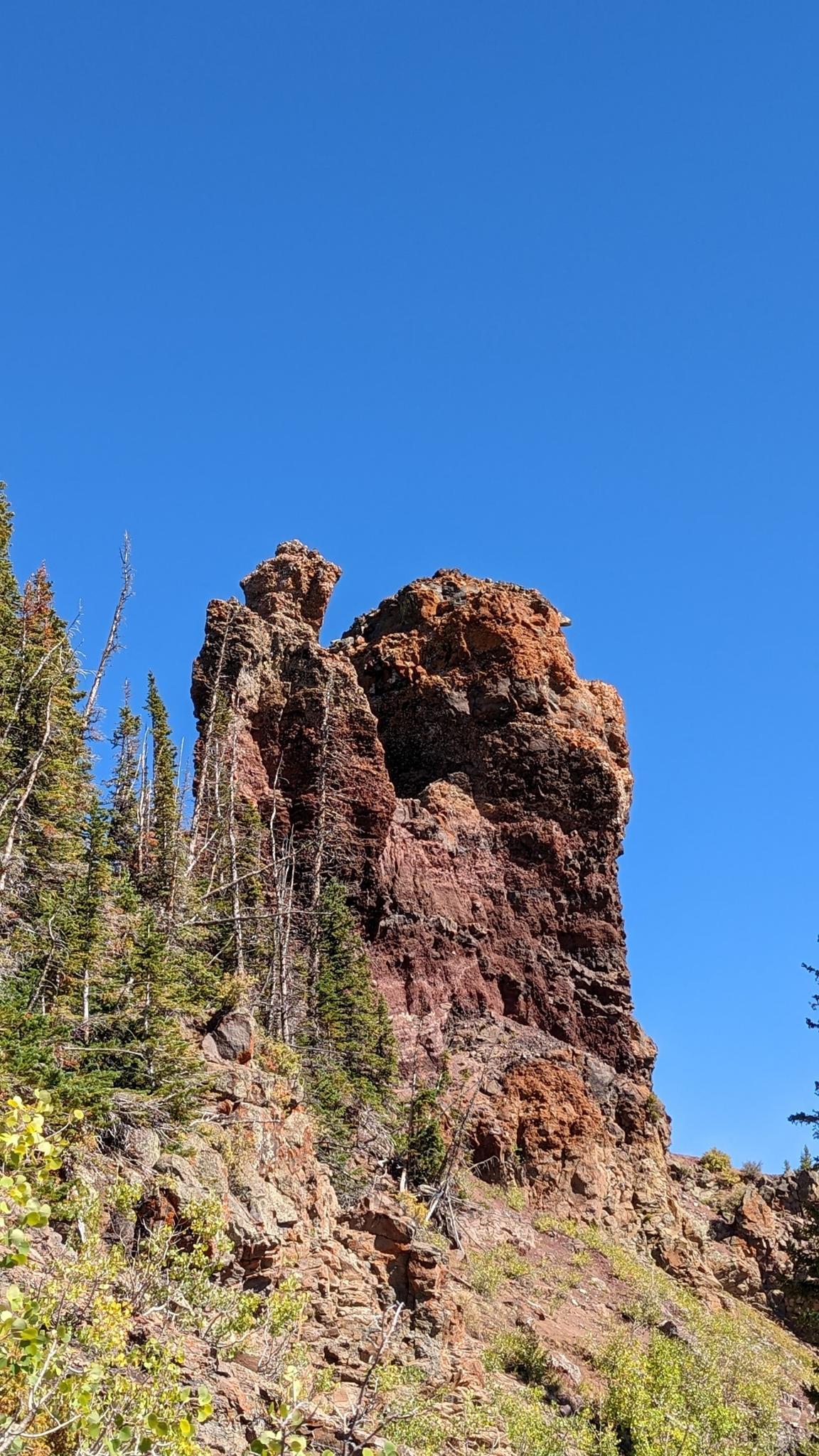 Tall, reddish-brown rock formation stands against a clear blue sky.