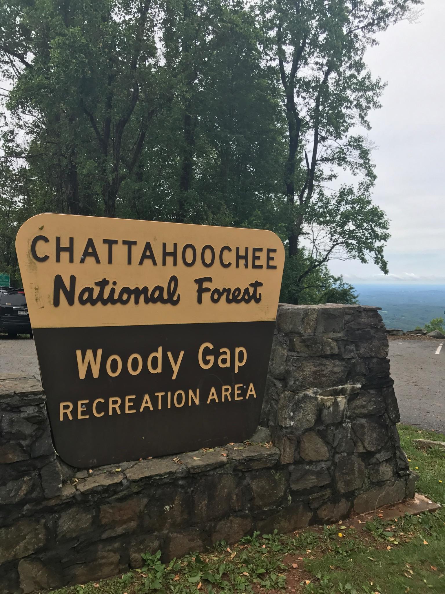 A brown and yellow sign on a stone base, trees behind.
