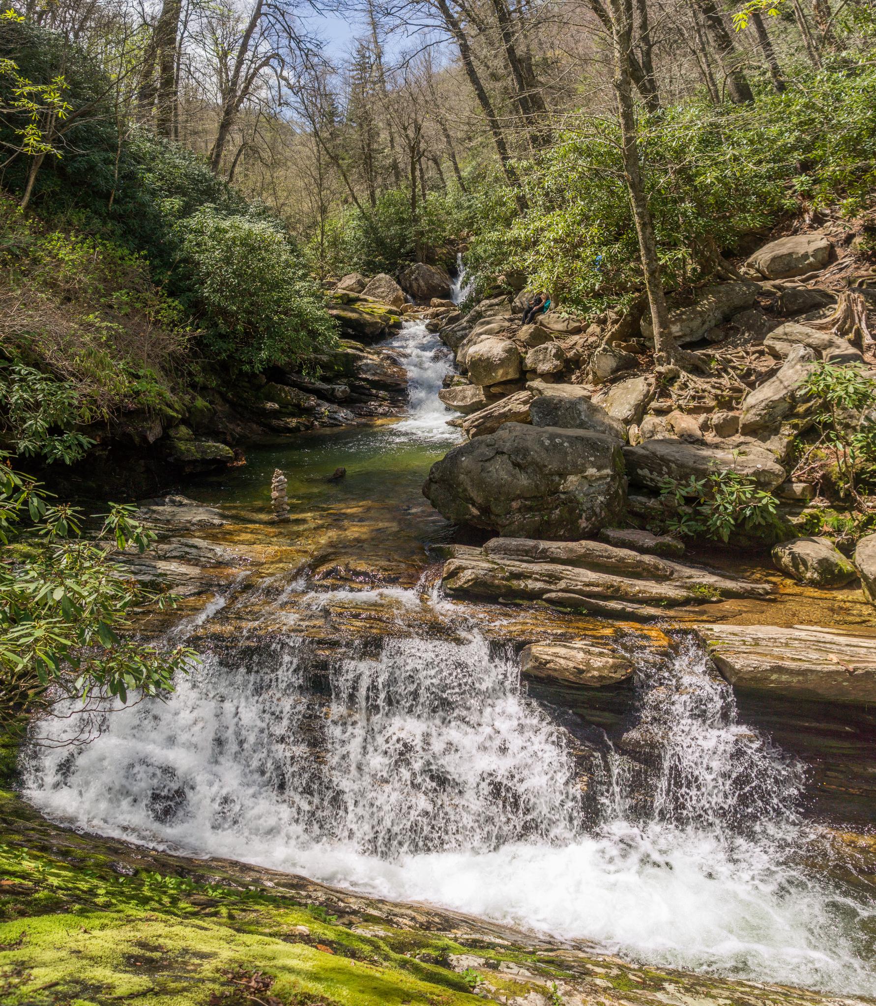Cascading waterfall over rocks in a lush, green forest on a sunny day.