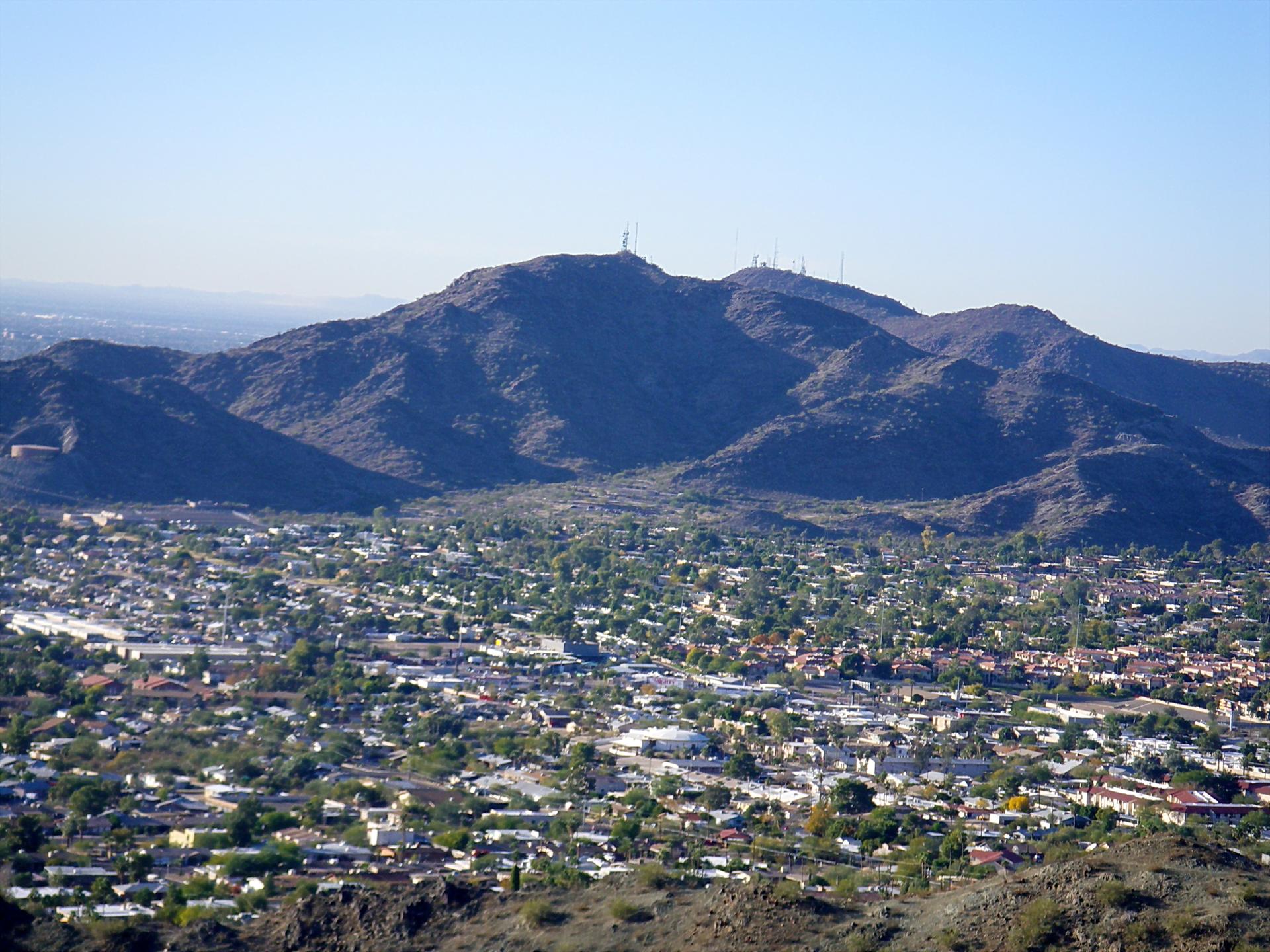 Bright daylight view of a city at the base of large, dark mountains.