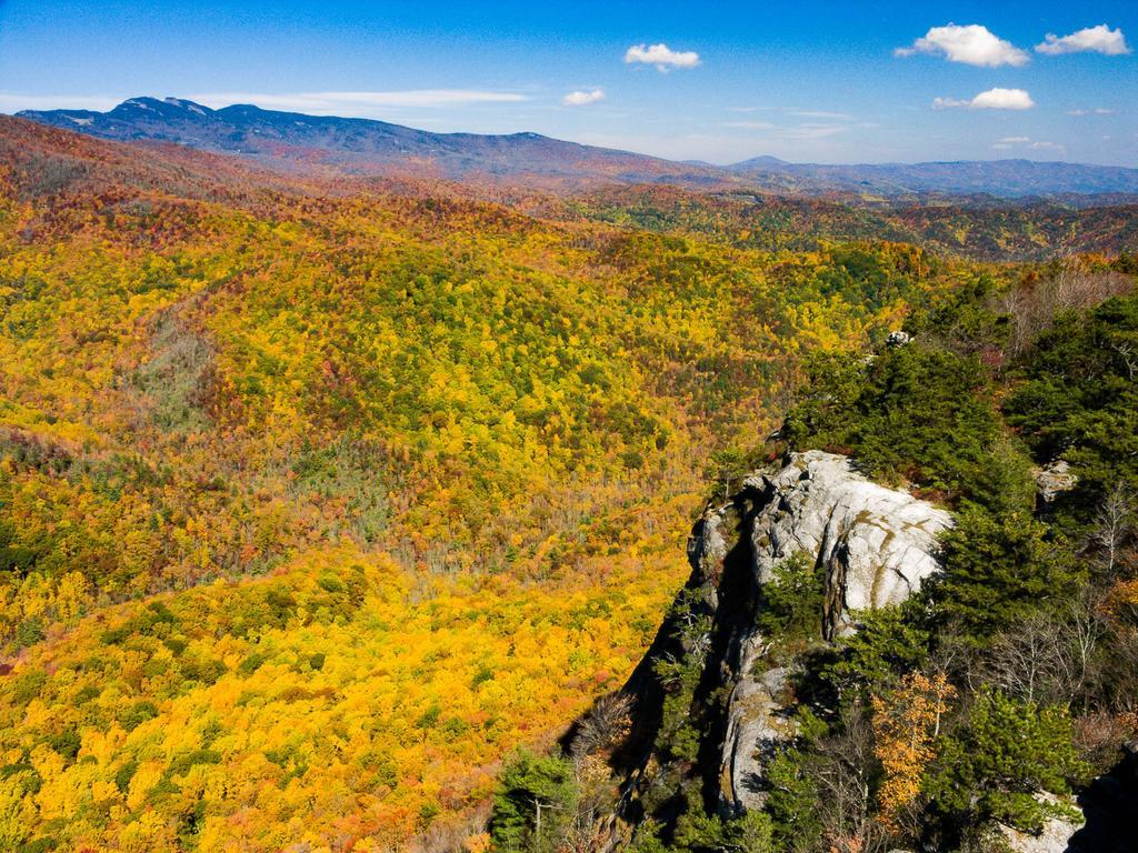 Vast mountain landscape with vibrant yellow and orange autumn foliage, rocky outcrop.