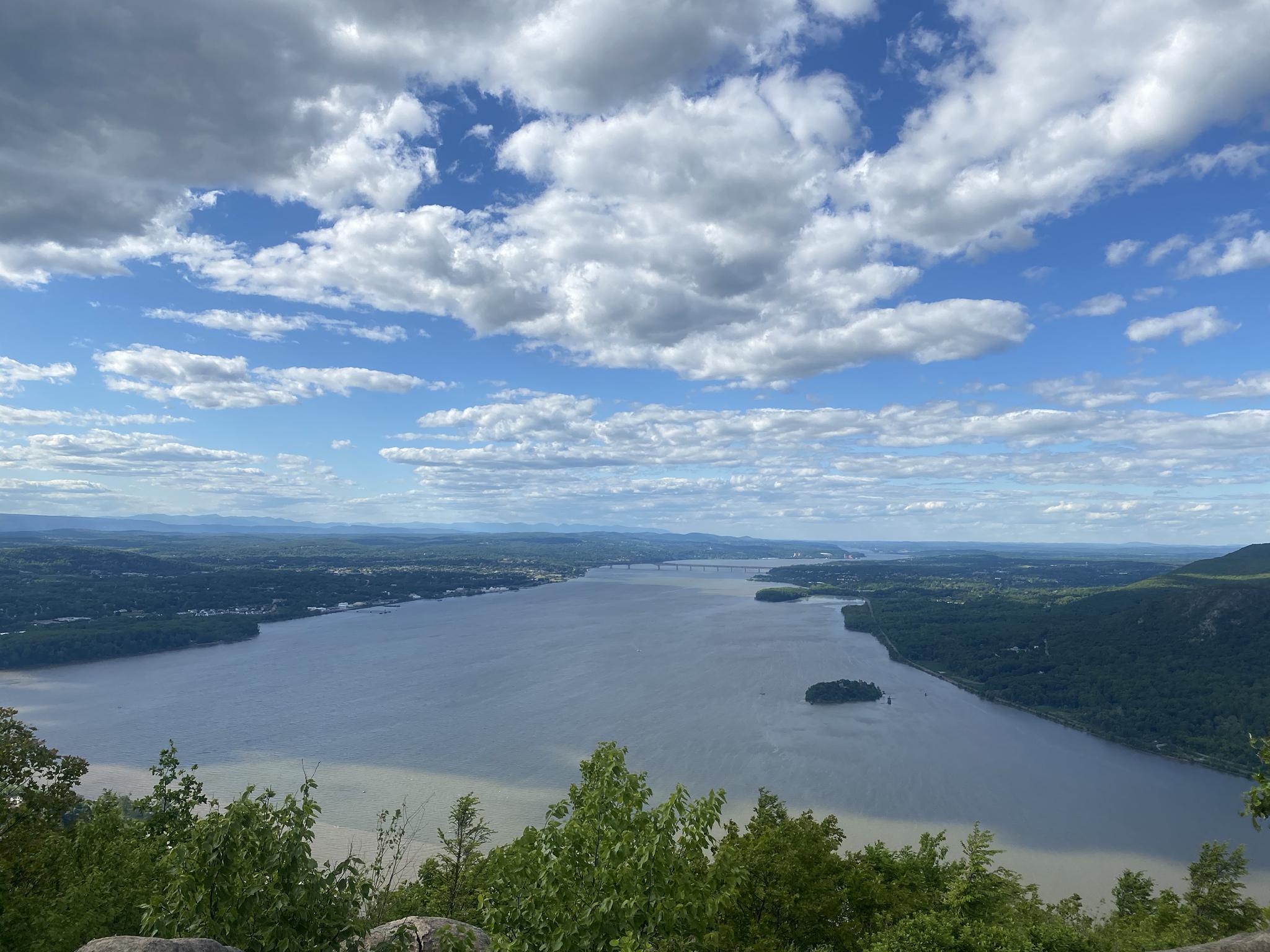 Panoramic view of a wide river winding through green forested hills under a cloudy sky.