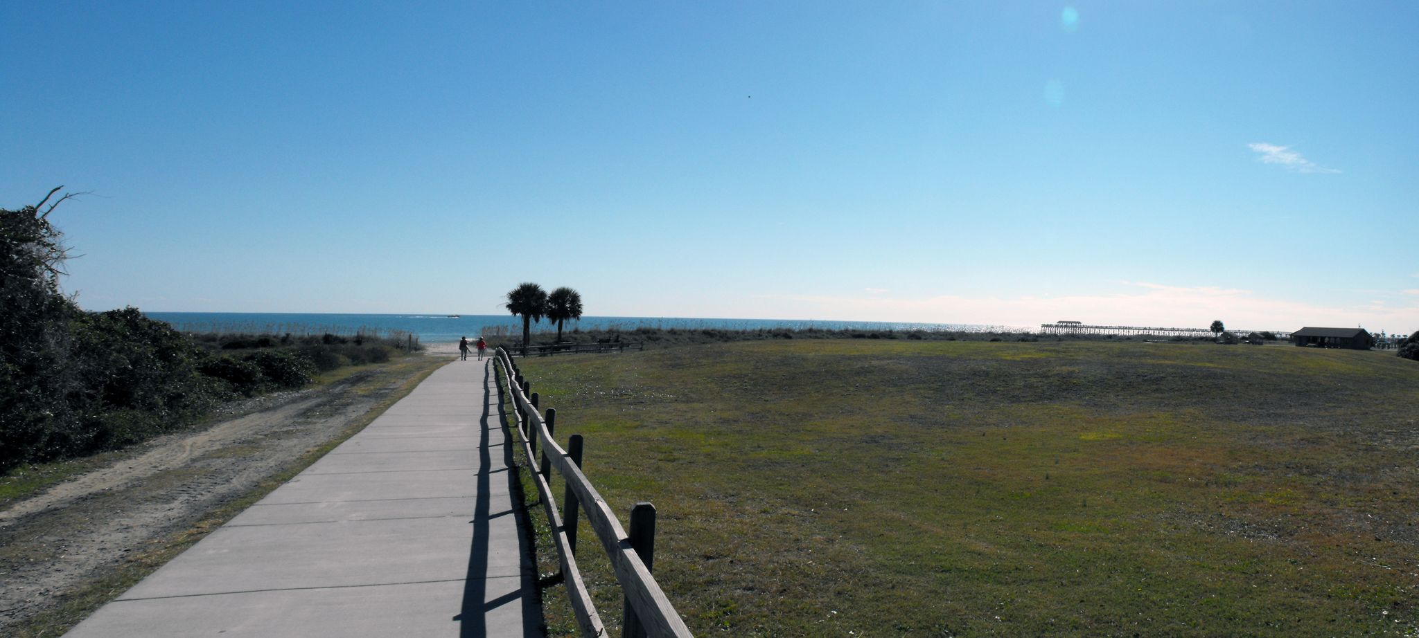 Paved path leading to a sunny beach with palm trees and ocean. - Myrtle Beach State Park to Boardwalk Beach Walk