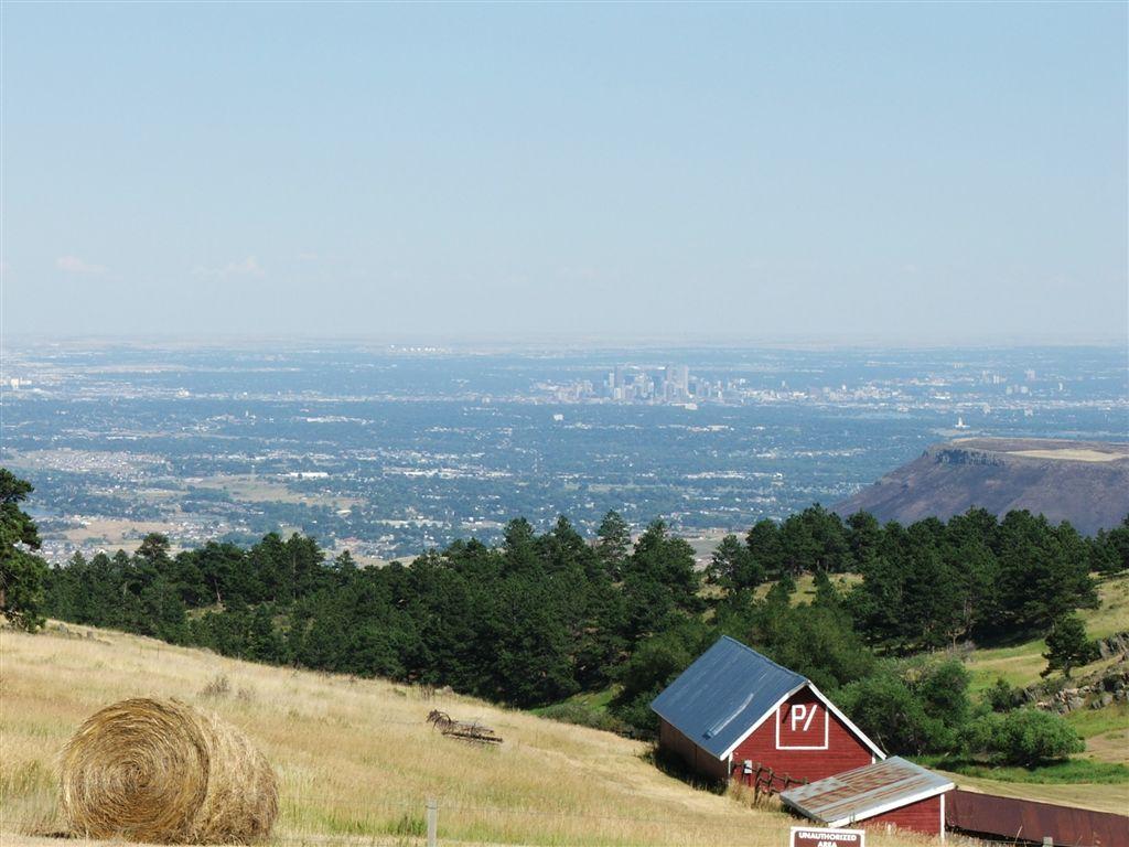 Red barn and hay bales on a hill overlooking a distant city.