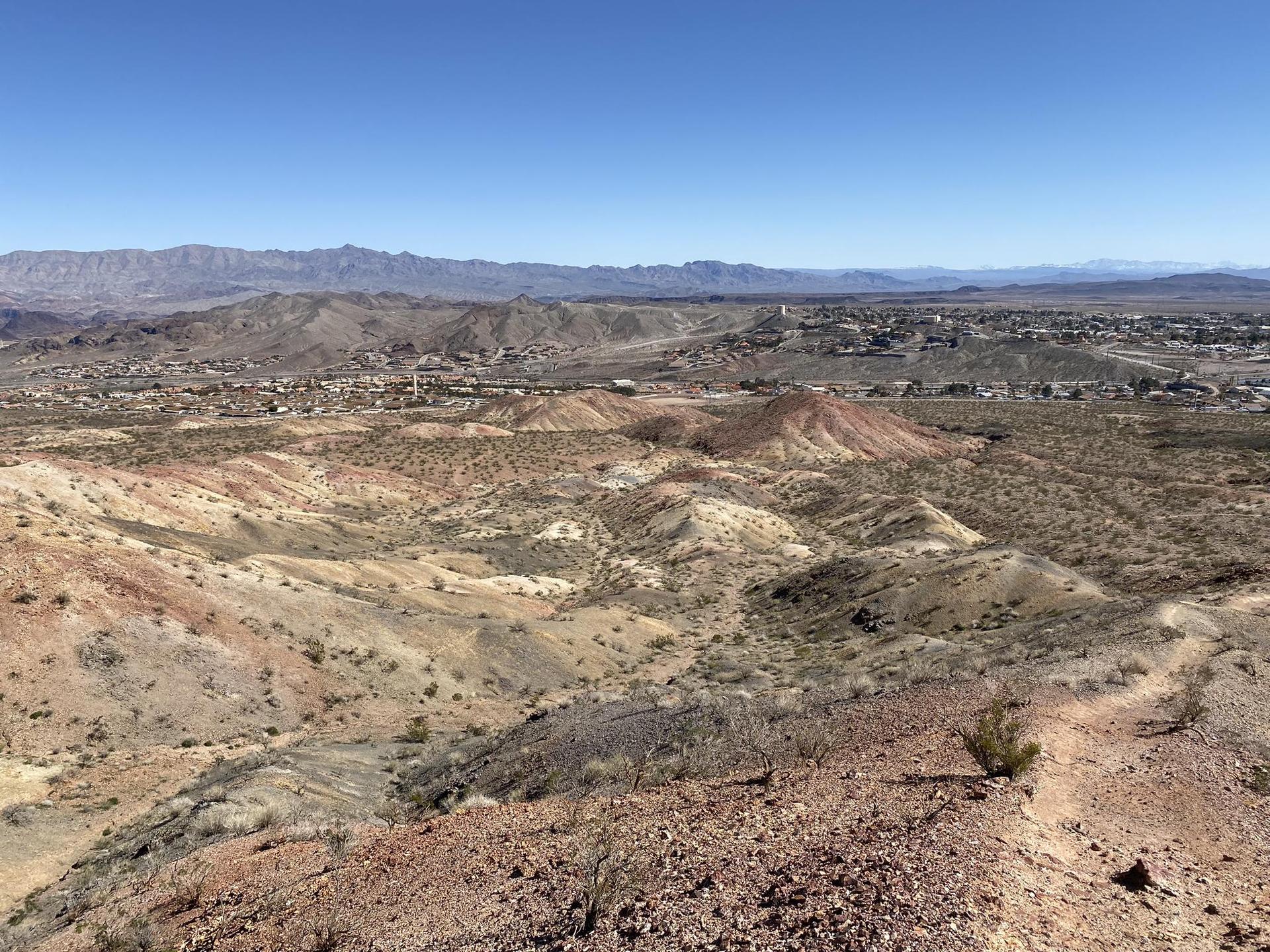 Vast desert landscape with colorful hills and a distant town under a clear blue sky.