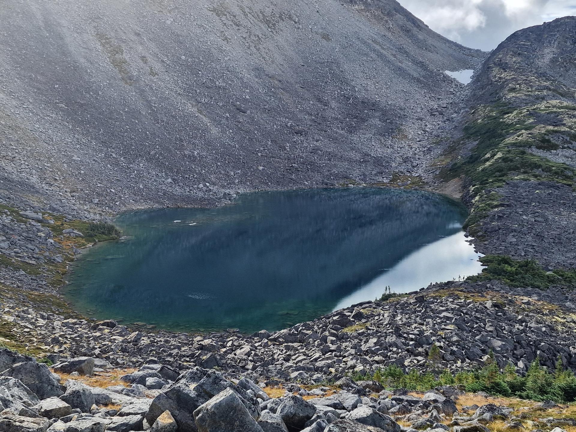 Dark blue alpine lake surrounded by rocky mountain slopes, overcast light.