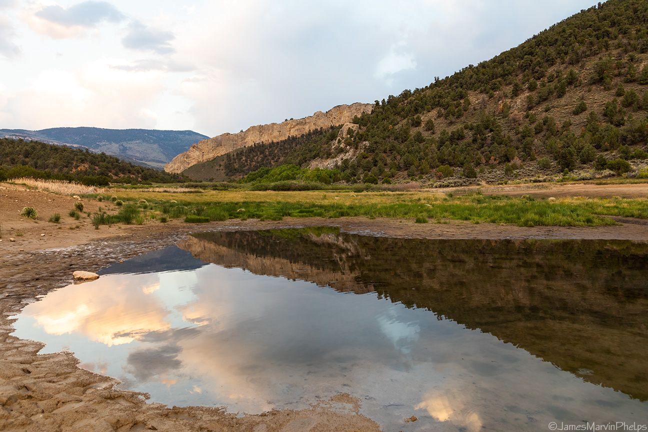 Pond reflecting cloudy sky, surrounded by arid valley and distant mountains. - Cave Springs Loop Trail