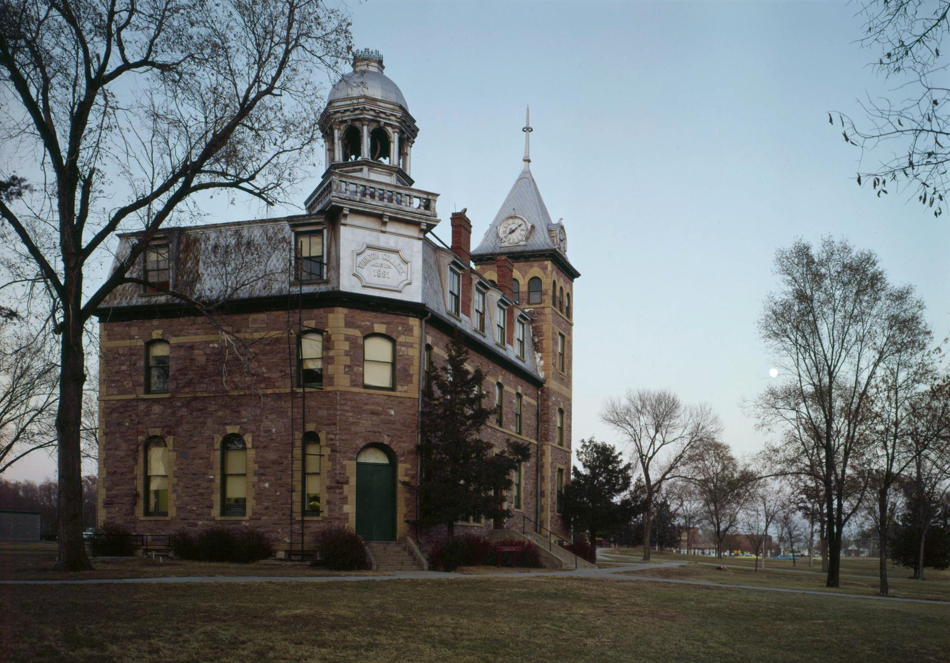Historic brick building with two towers and bare trees under a soft sky.